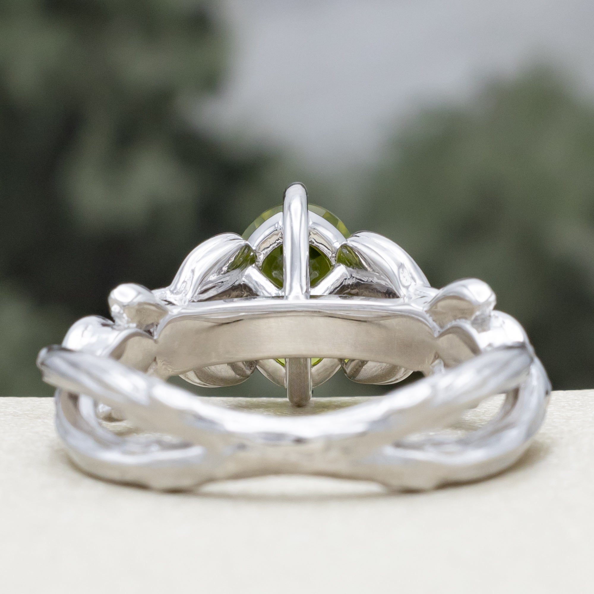 White gold ring with a green peridot on a blurred natural background