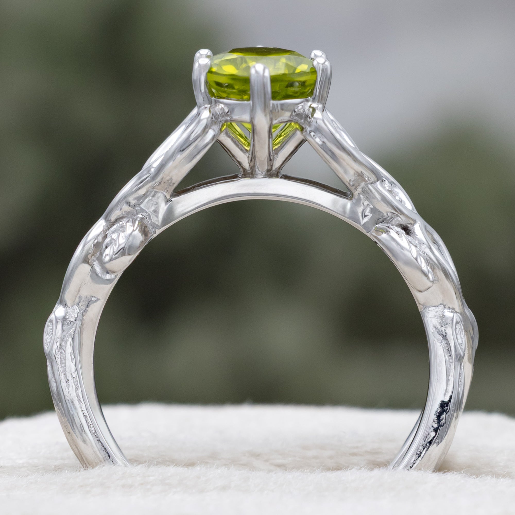 White gold ring with a green peridot on a blurred natural background