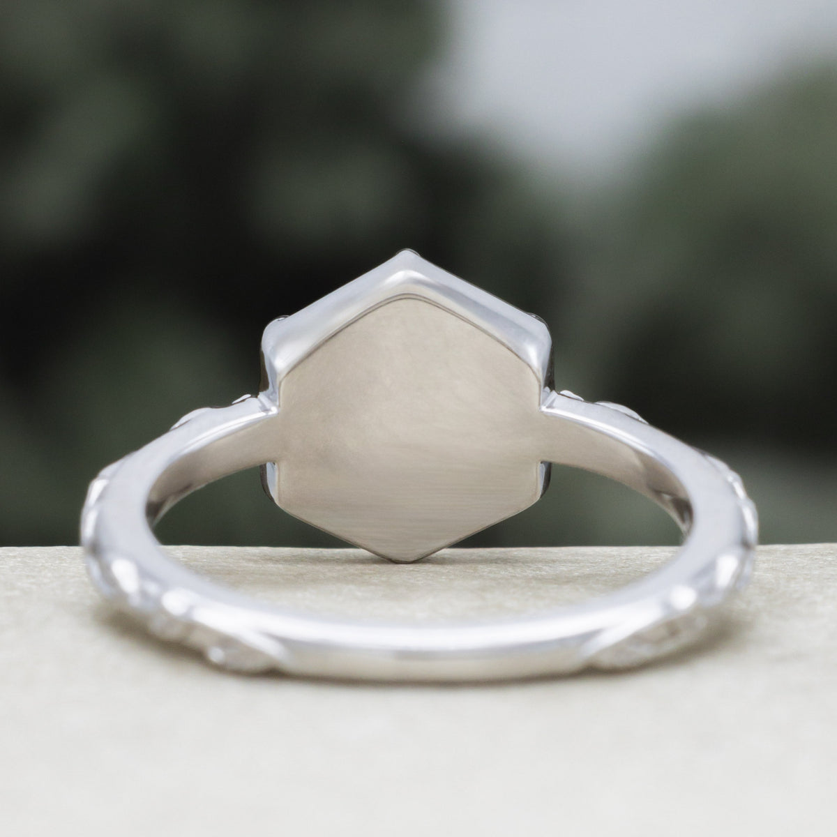 White gold engagement ring with vine band against a blurred green background