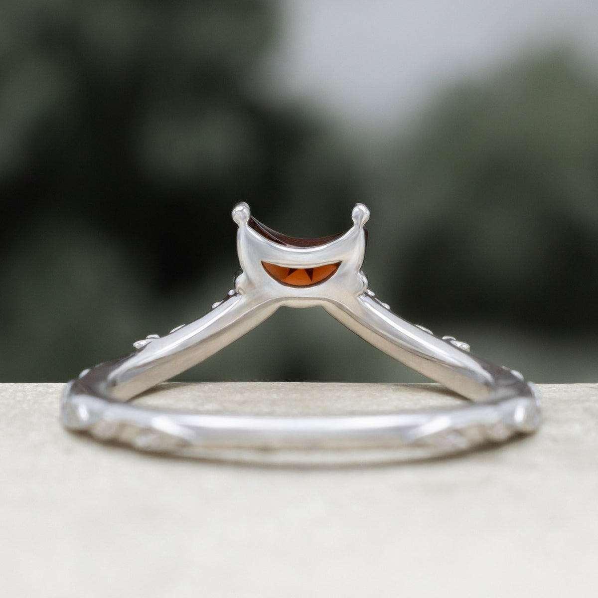 White gold crescent moon garnet tracer with vine band and black diamond accents against a blurred green background