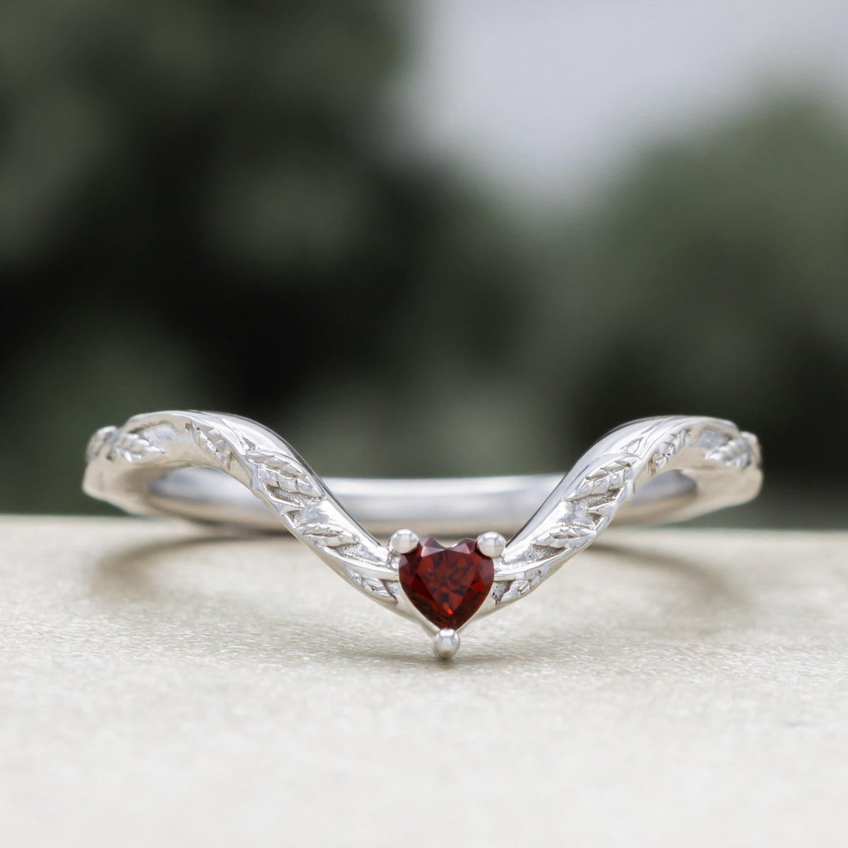White gold heart garnet tracer with vine band against a blurred green background
