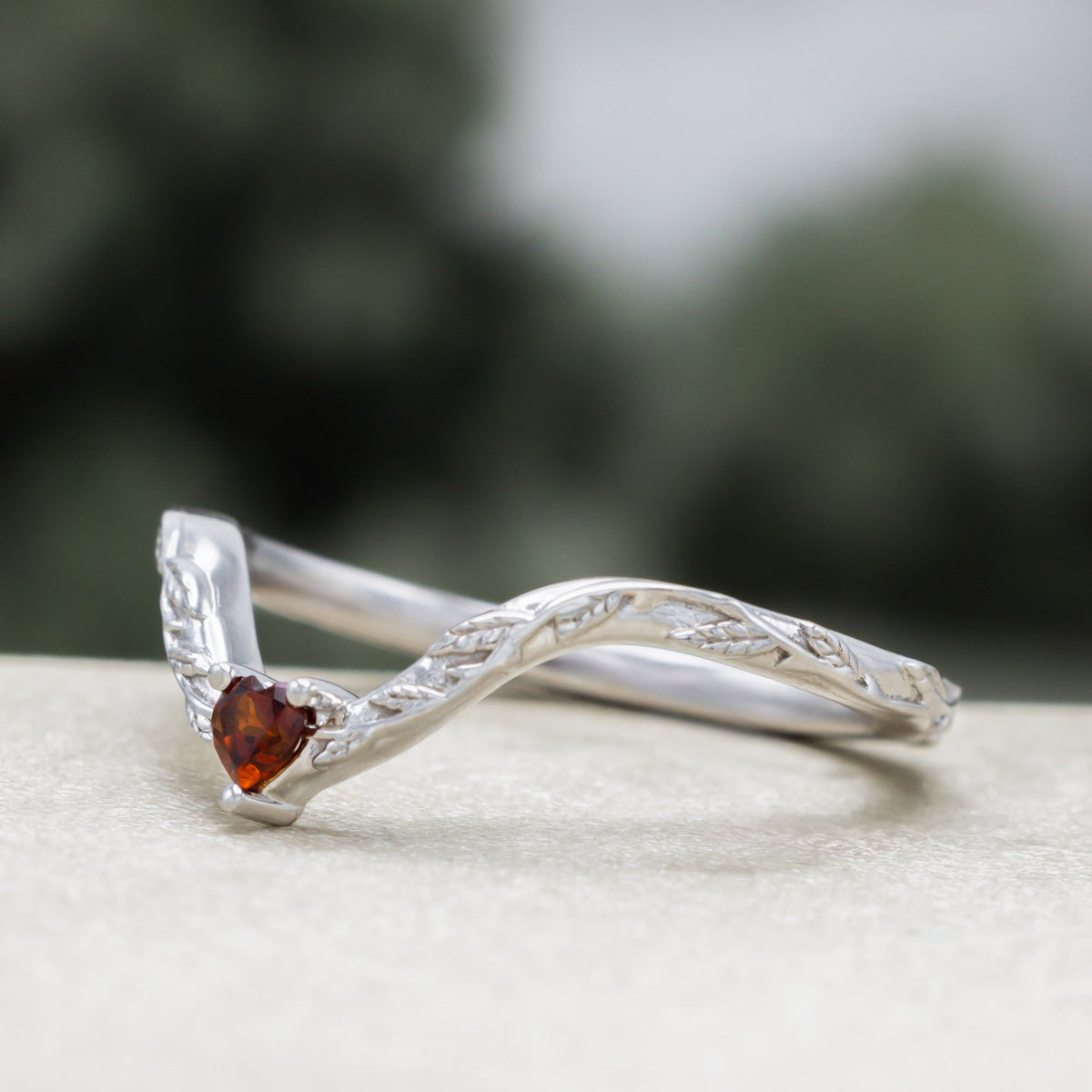 White gold heart garnet tracer with vine band against a blurred green background