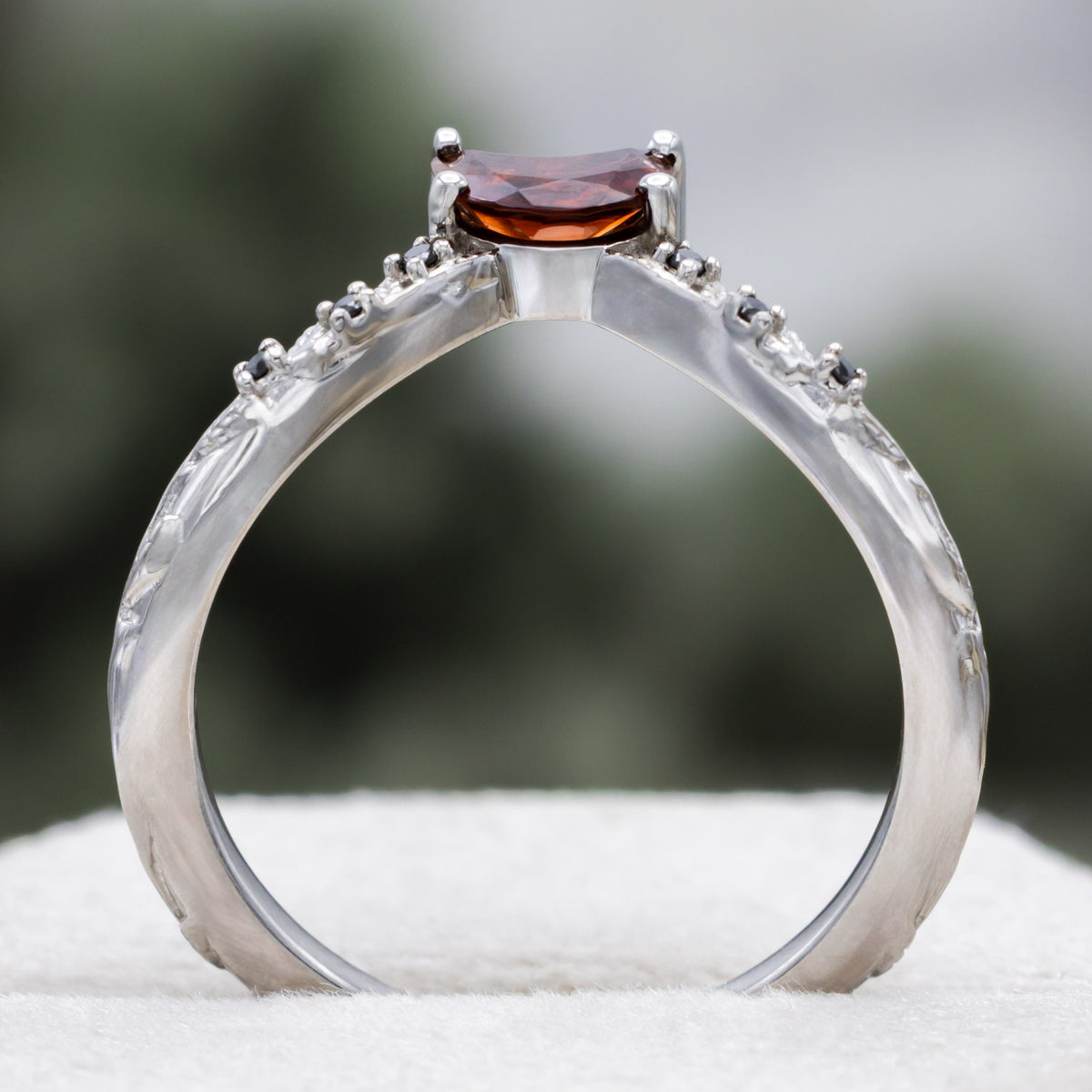 White gold crescent moon garnet tracer with vine band and black diamond accents against a blurred green background
