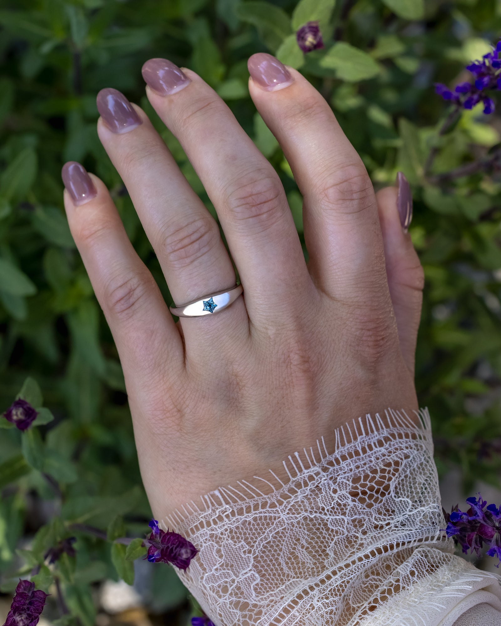 Hand wearing a white gold ring with a star shaped sapphire against a blurred natural background