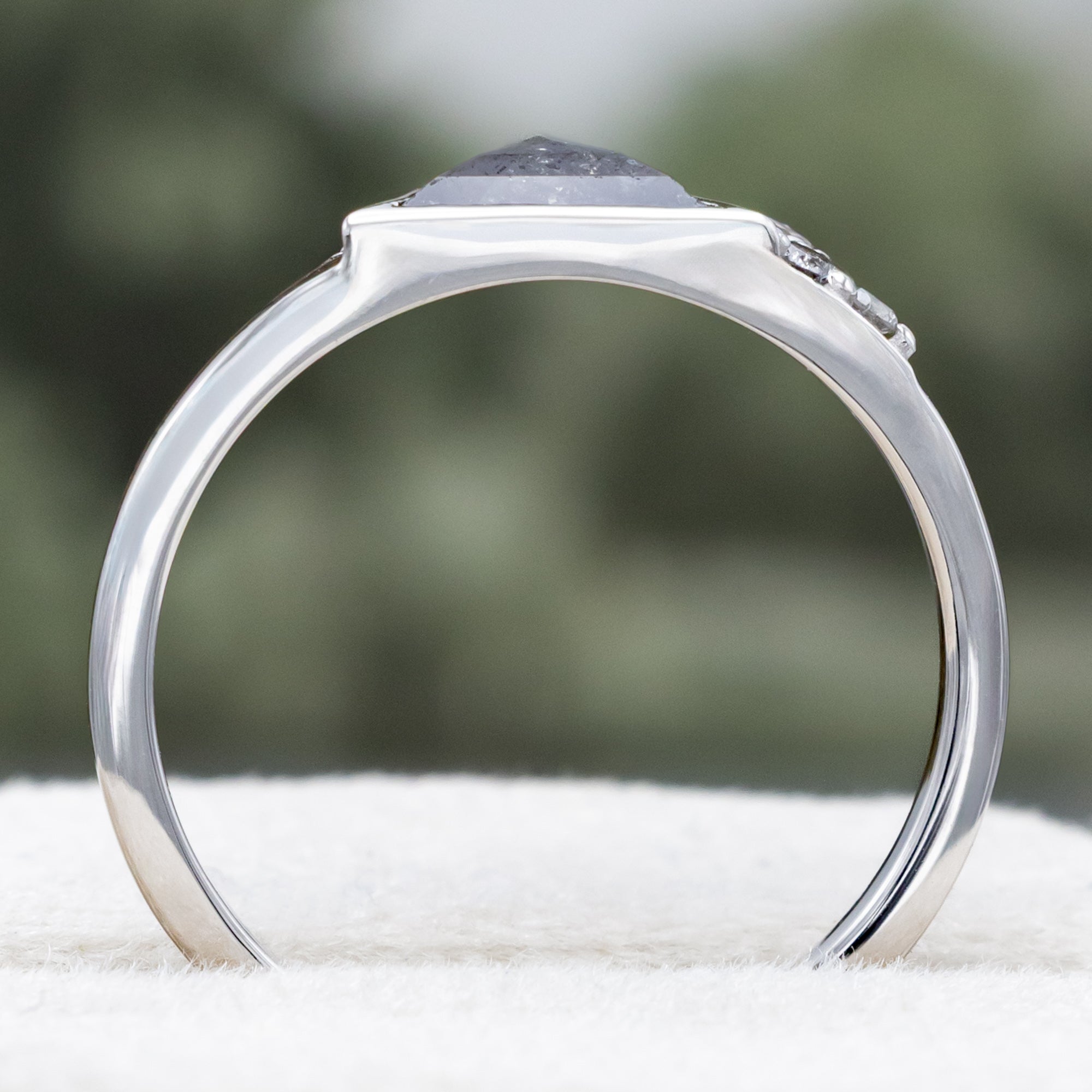 White gold ring with salt & pepper diamond center stone and diamond accents on a blurred background