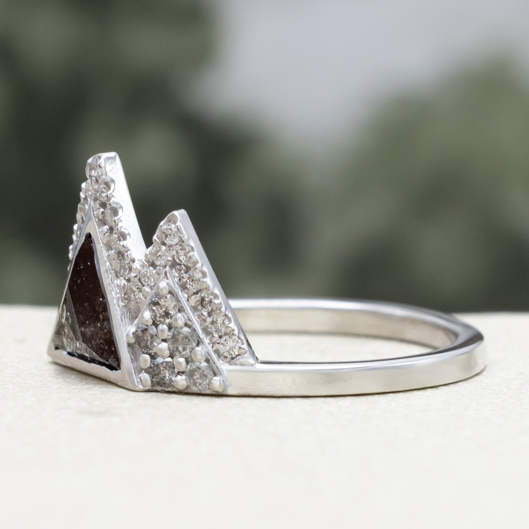 White gold ring with salt & pepper diamond center stone and diamond accents on a blurred background