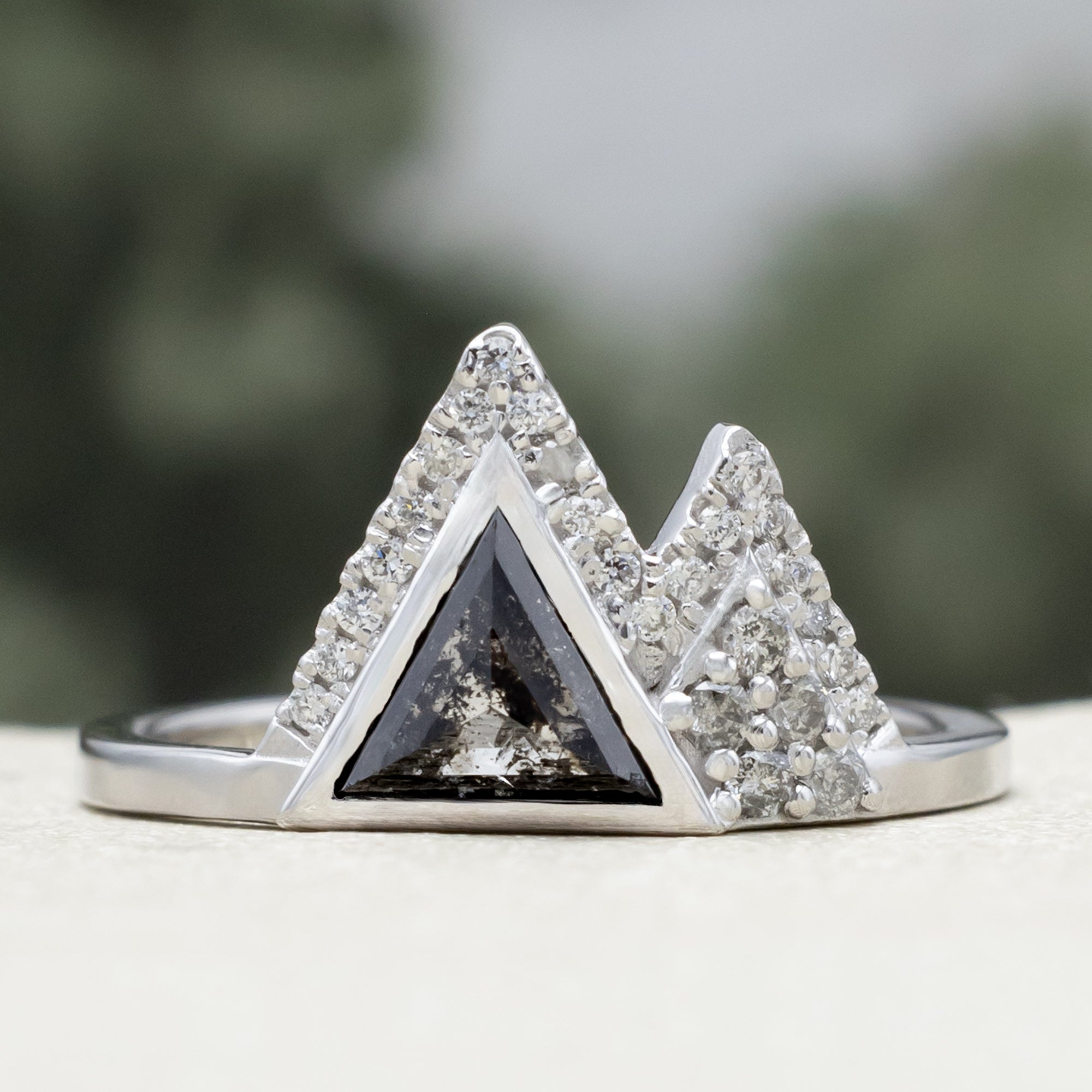 White gold ring with salt & pepper diamond center stone and diamond accents on a blurred background