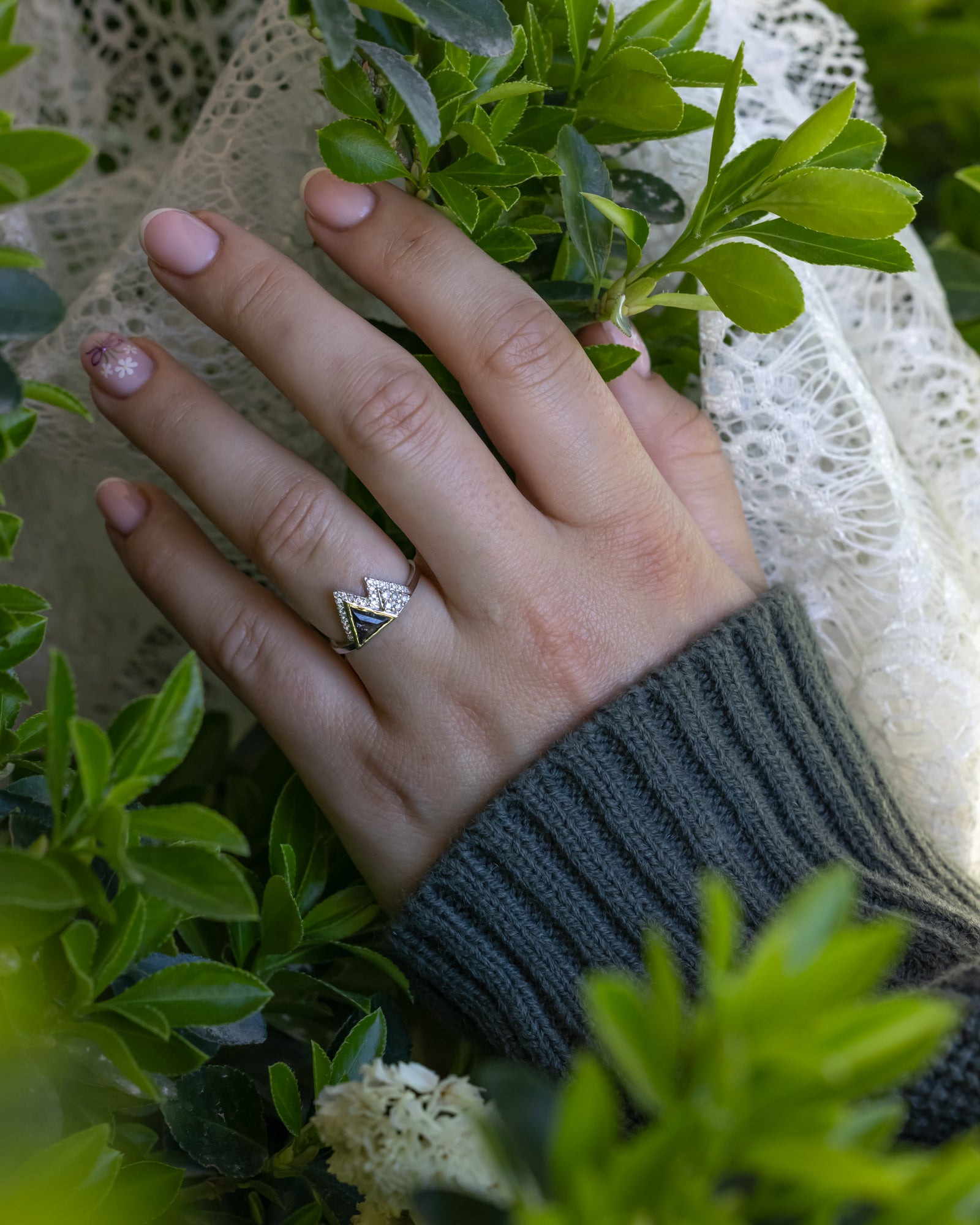 Hand wearing a ring with greenery and lace in the background