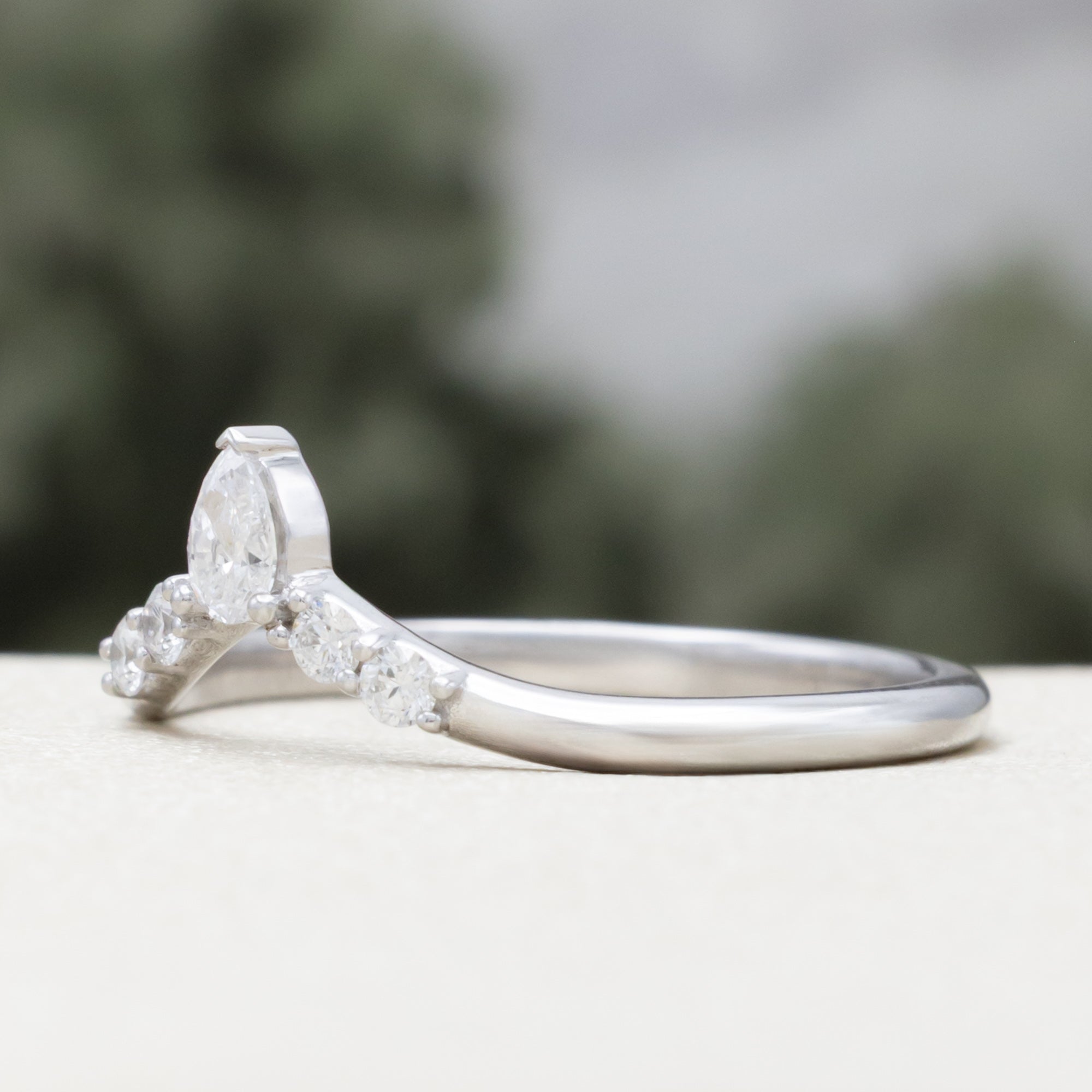 White gold ring with diamond accents on a blurred natural background