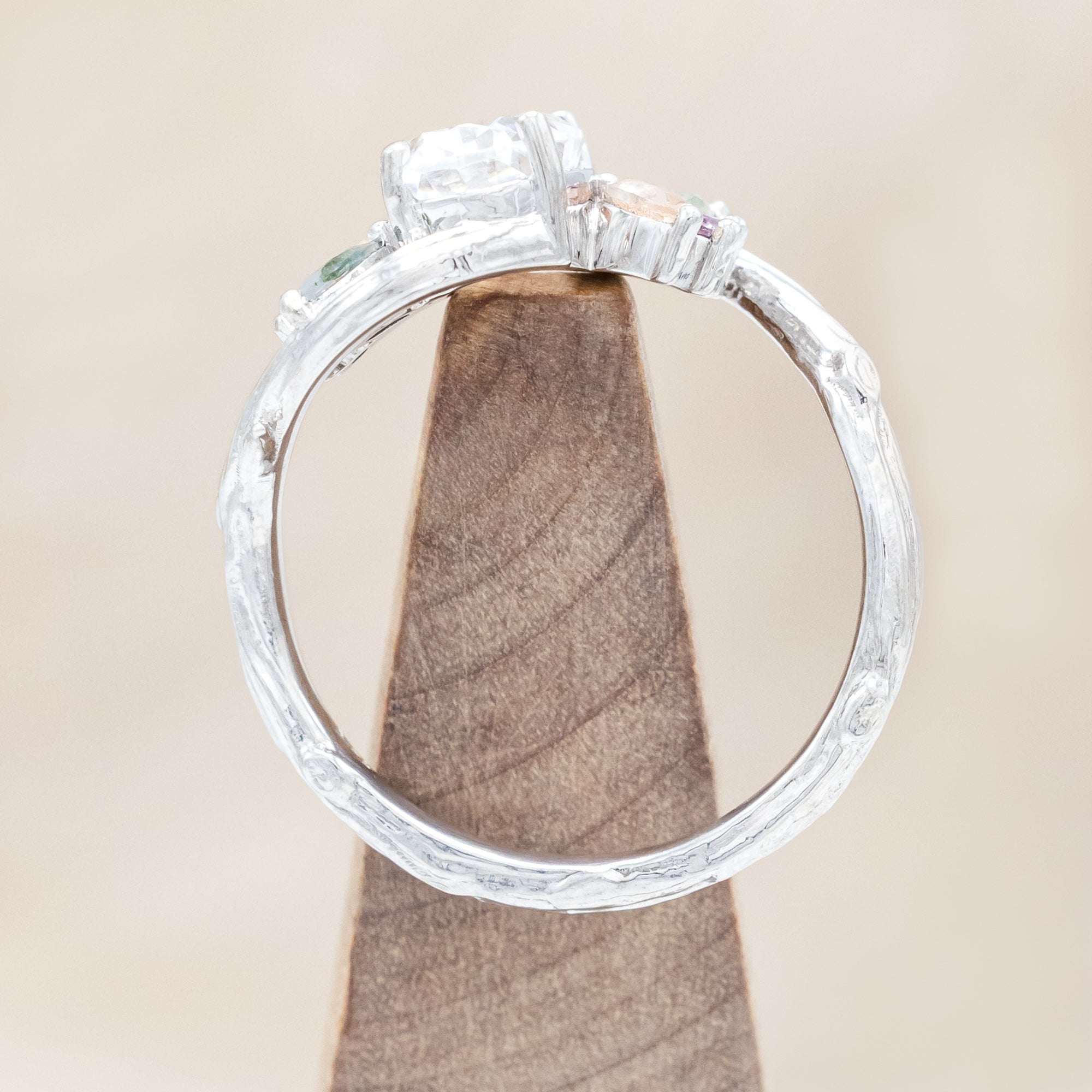 White gold ring with moissanite and smaller spinel, moss agate and sunstone accents on a wooden surface