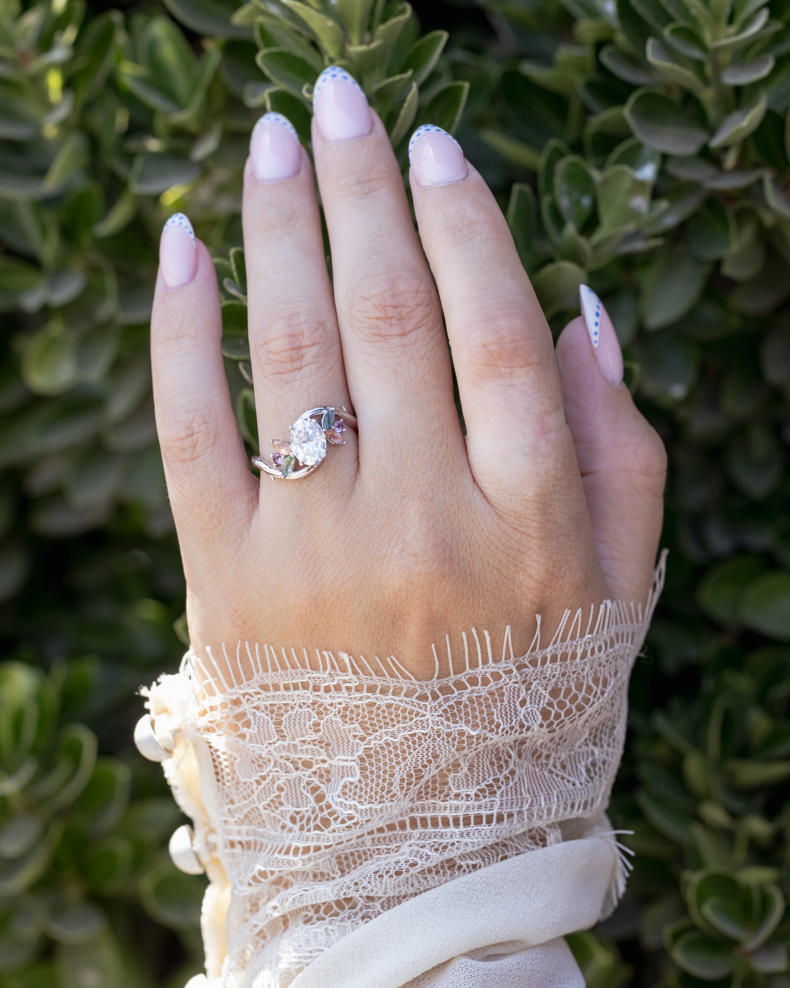 Hand wearing a moissanite ring with a blurred green leafy background