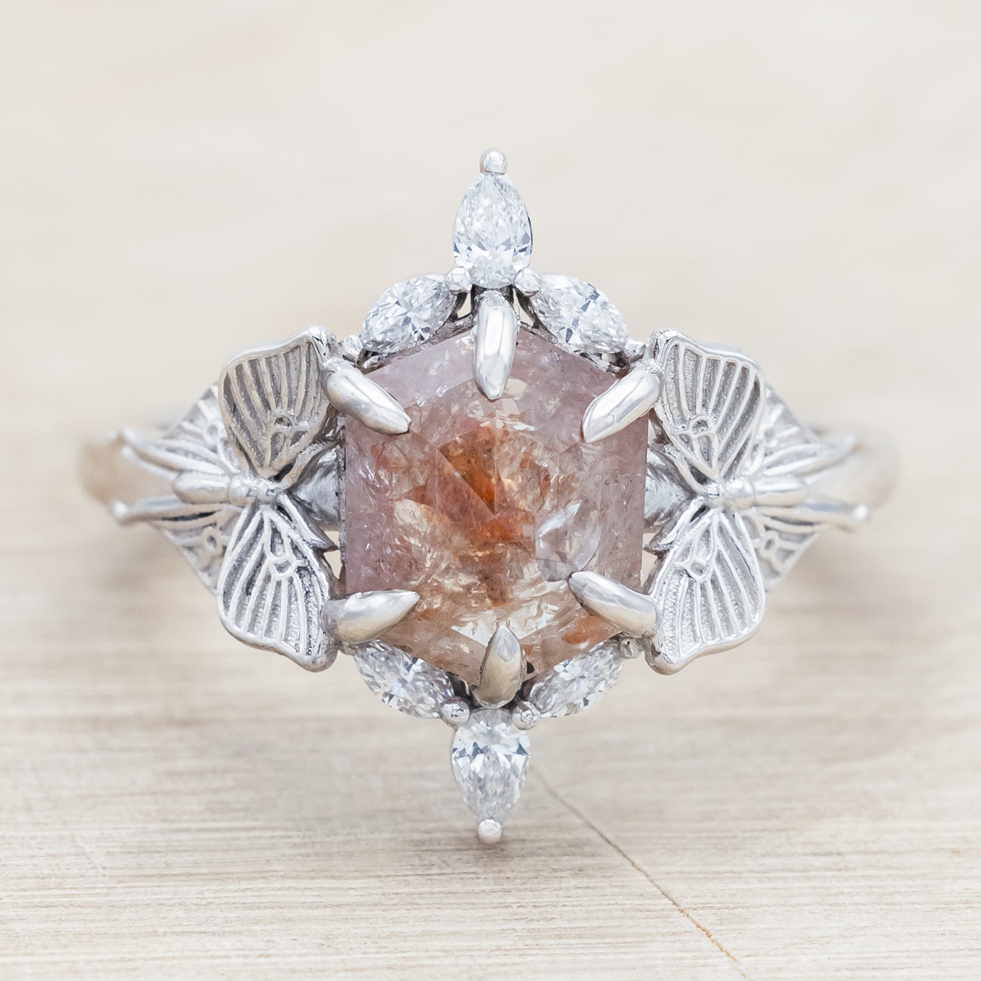 White gold ring with a salt & pepper diamond and moth design on a beige background