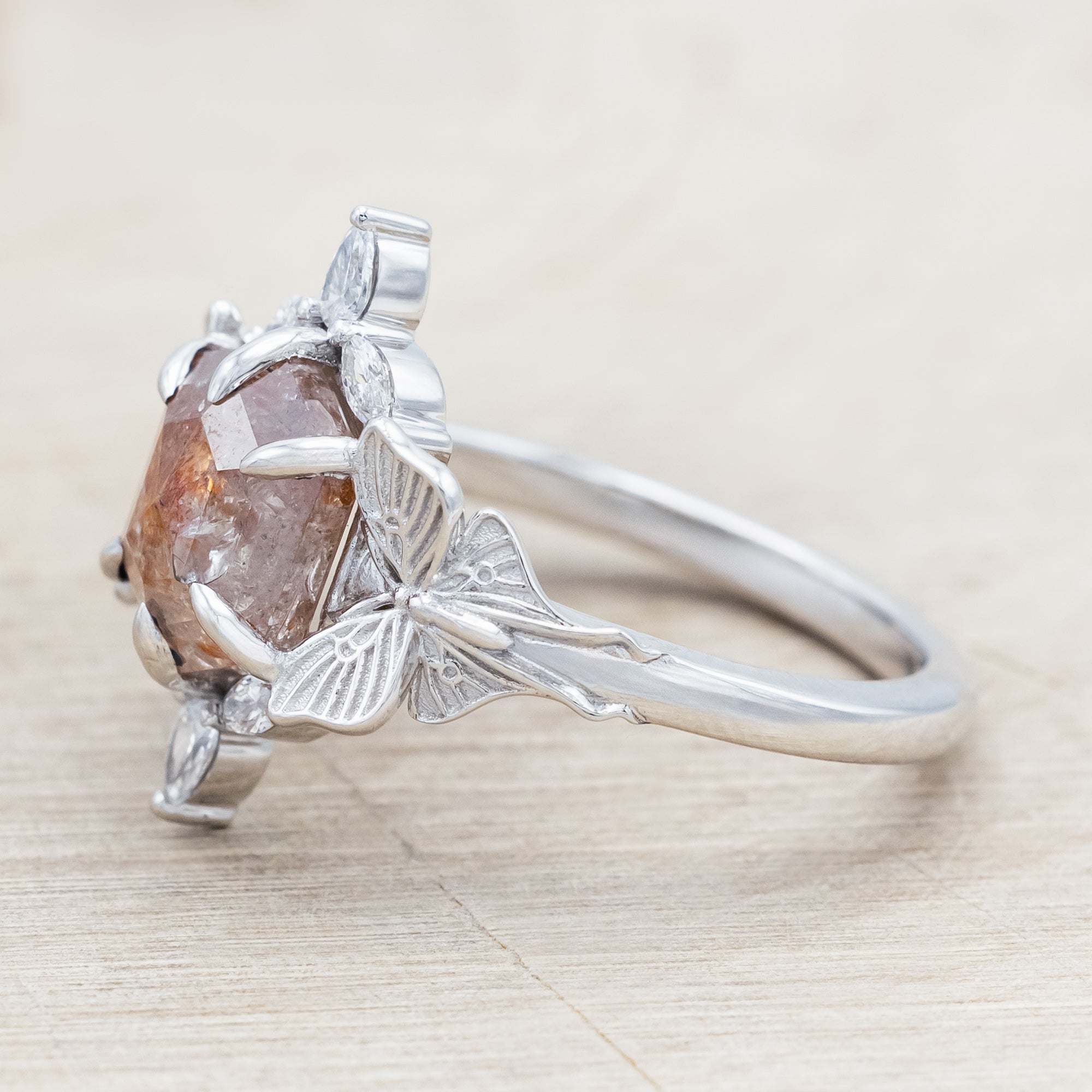 White gold ring with a salt & pepper diamond and moth design on a beige background