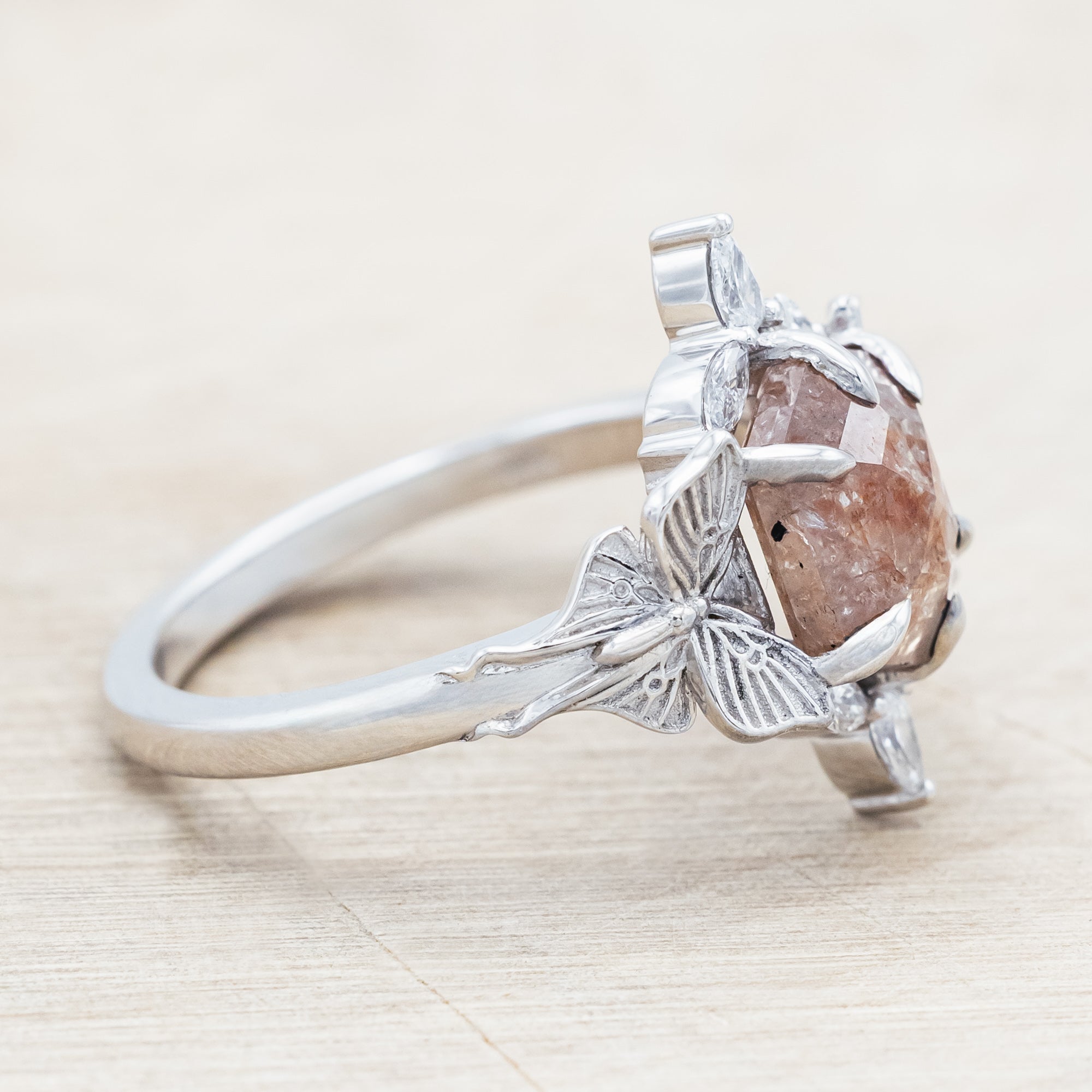 White gold ring with a salt & pepper diamond and moth design on a beige background