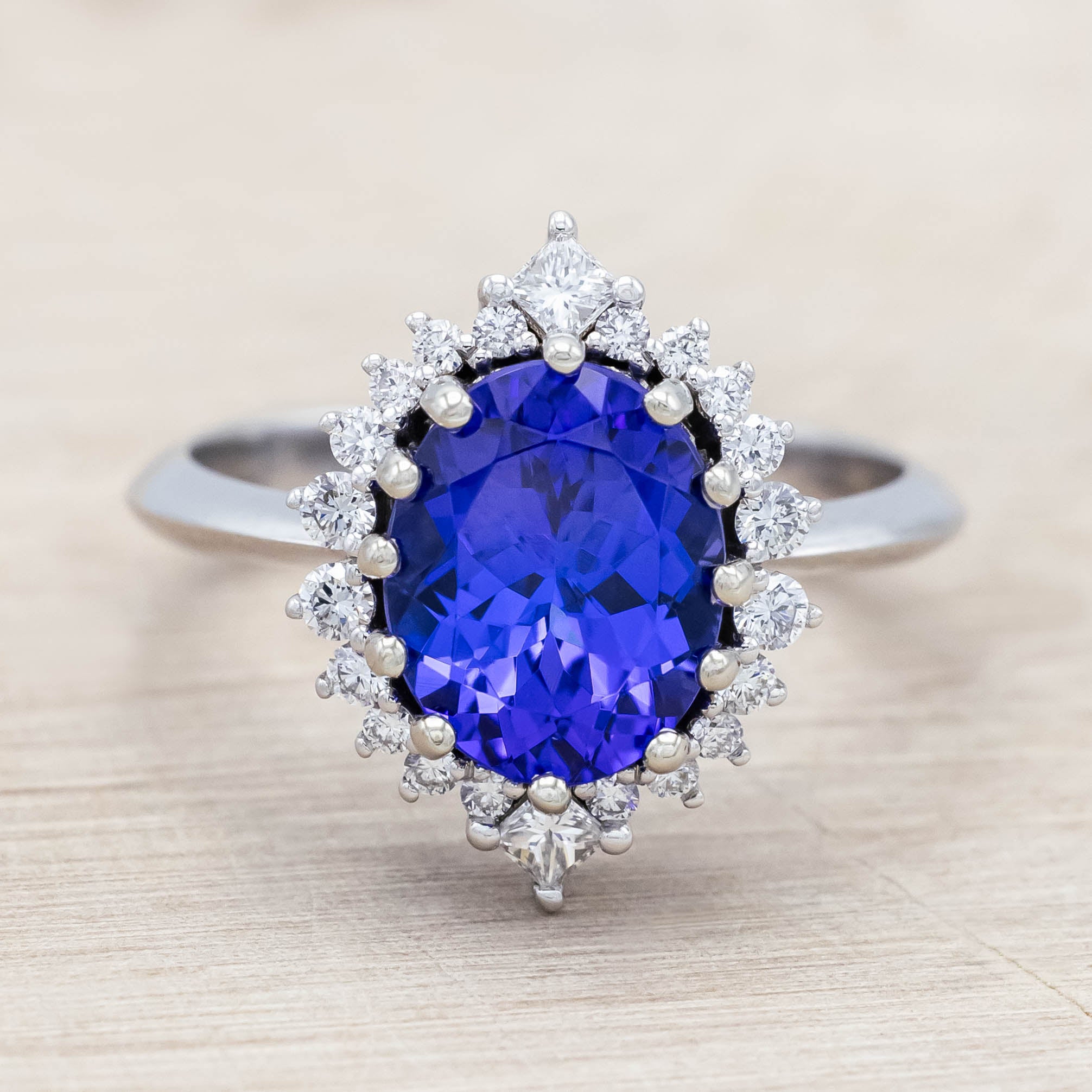 14K white gold ring with a blue tanzanite center stone and diamond halo on a beige background