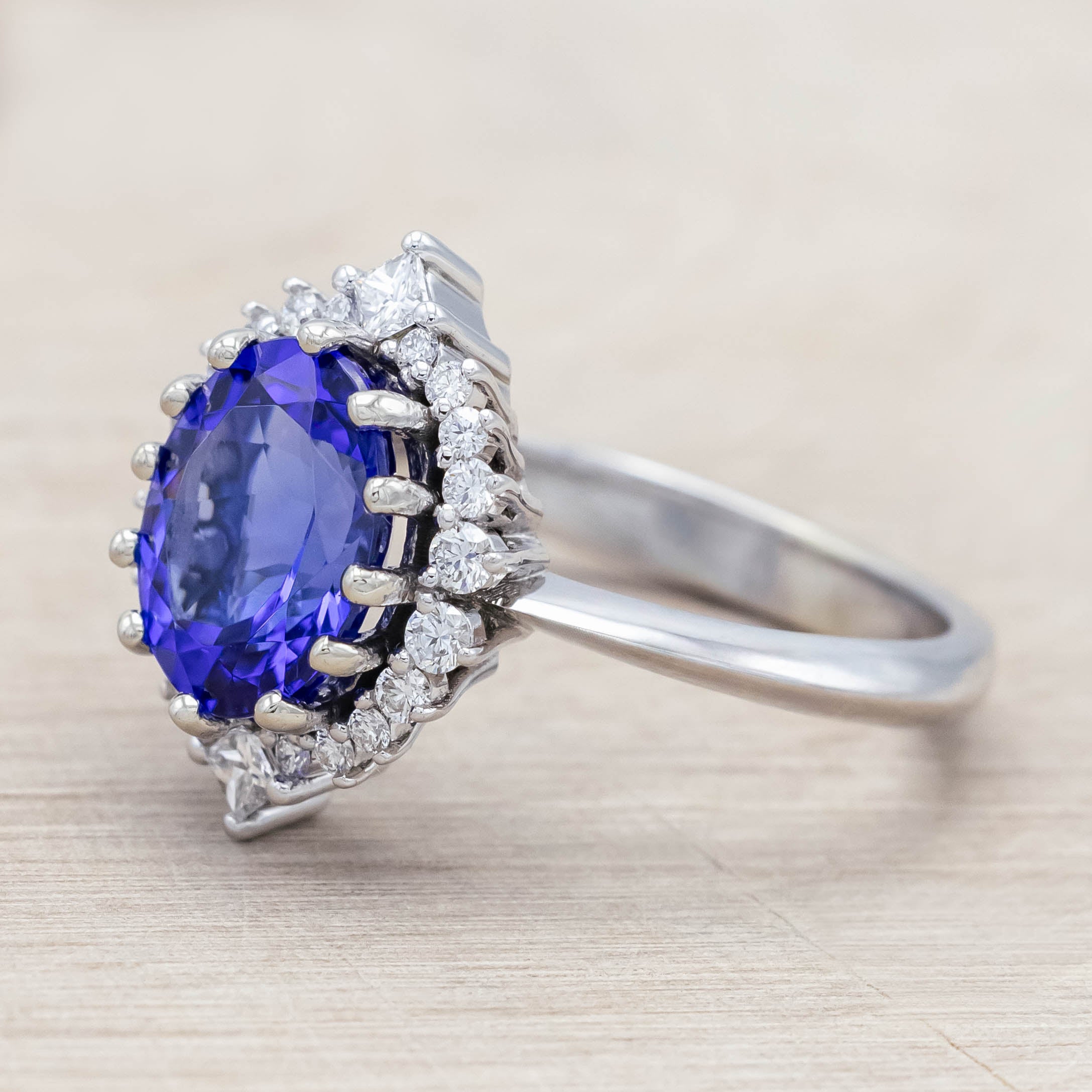 14K white gold ring with a blue tanzanite center stone and diamond halo on a beige background