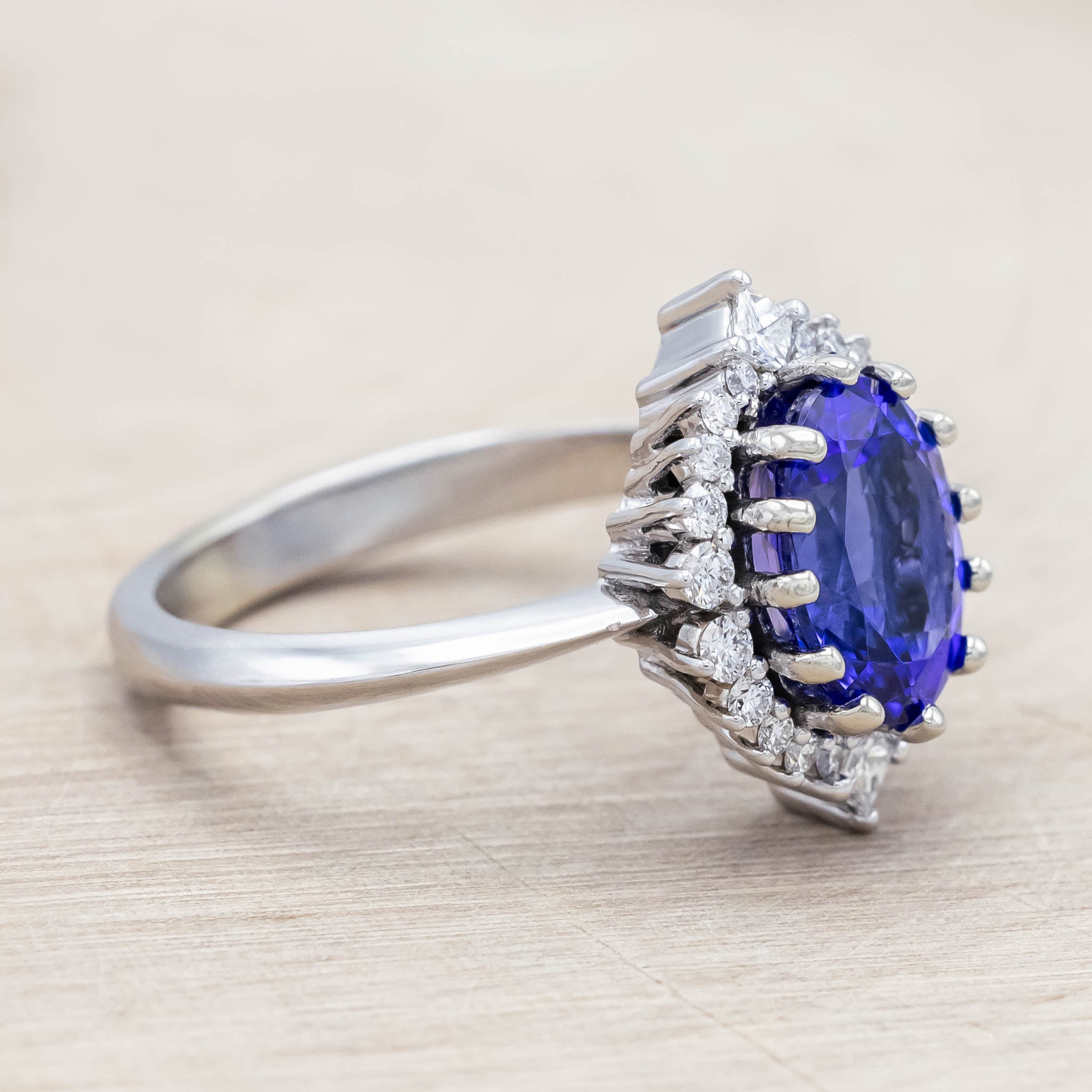 14K white gold ring with a blue Tanzanite center stone and diamond halo on a beige background