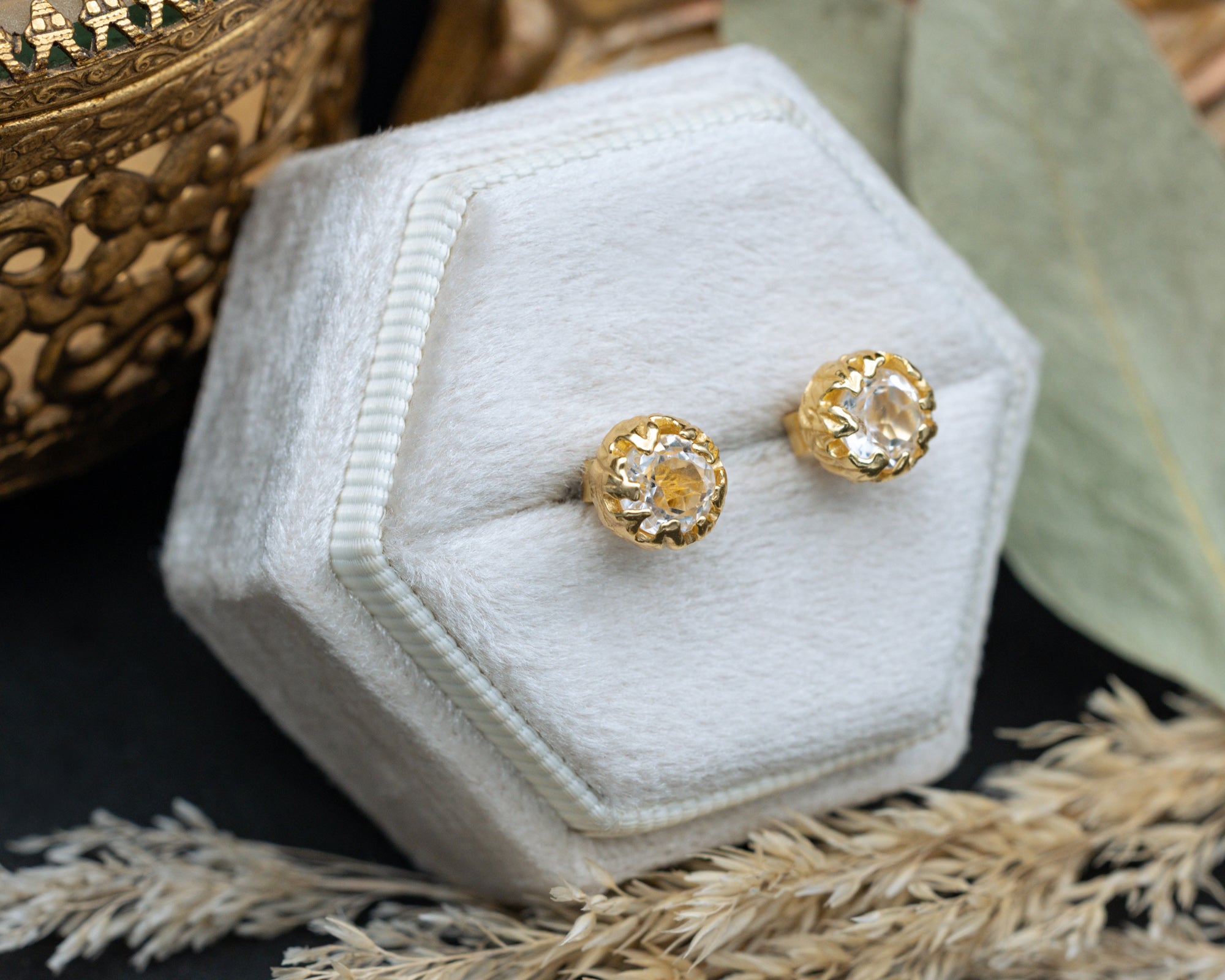 Gold white topaz earrings in a hexagonal white velvet box with decorative elements.