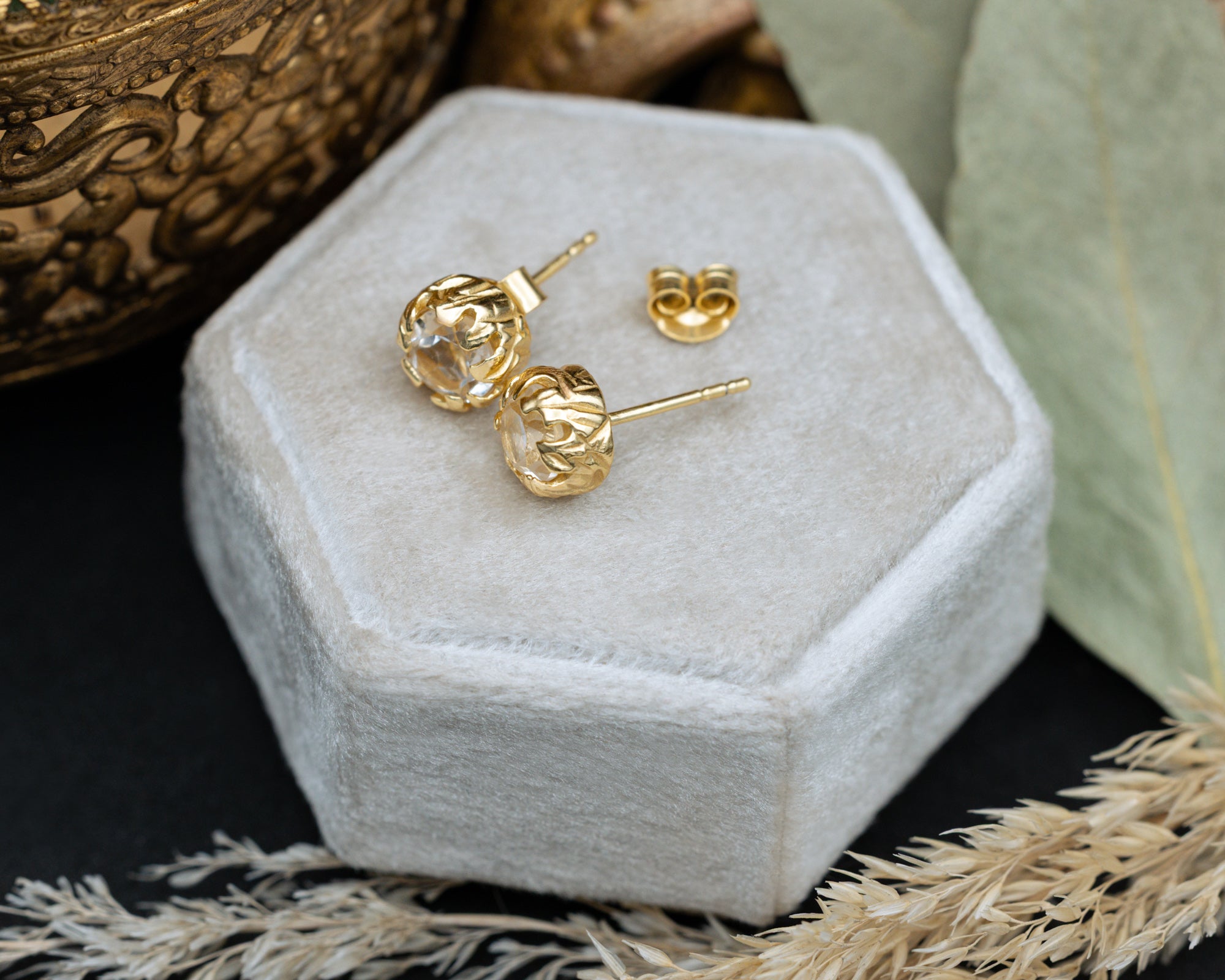 Gold topaz earrings on a white hexagonal jewelry box with decorative elements.