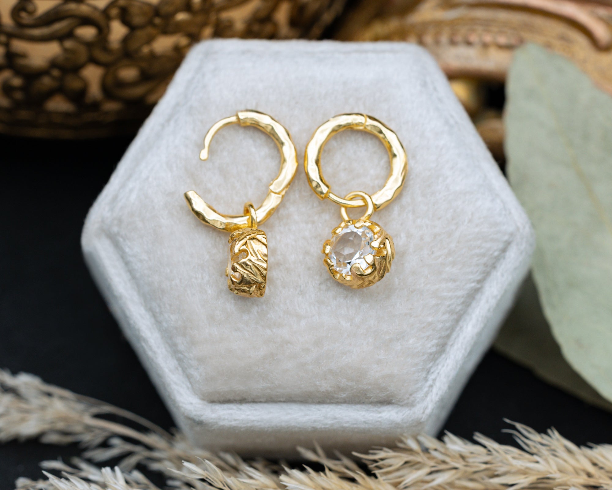 Gold hoop earrings with a white topaz on a white hexagonal stand.