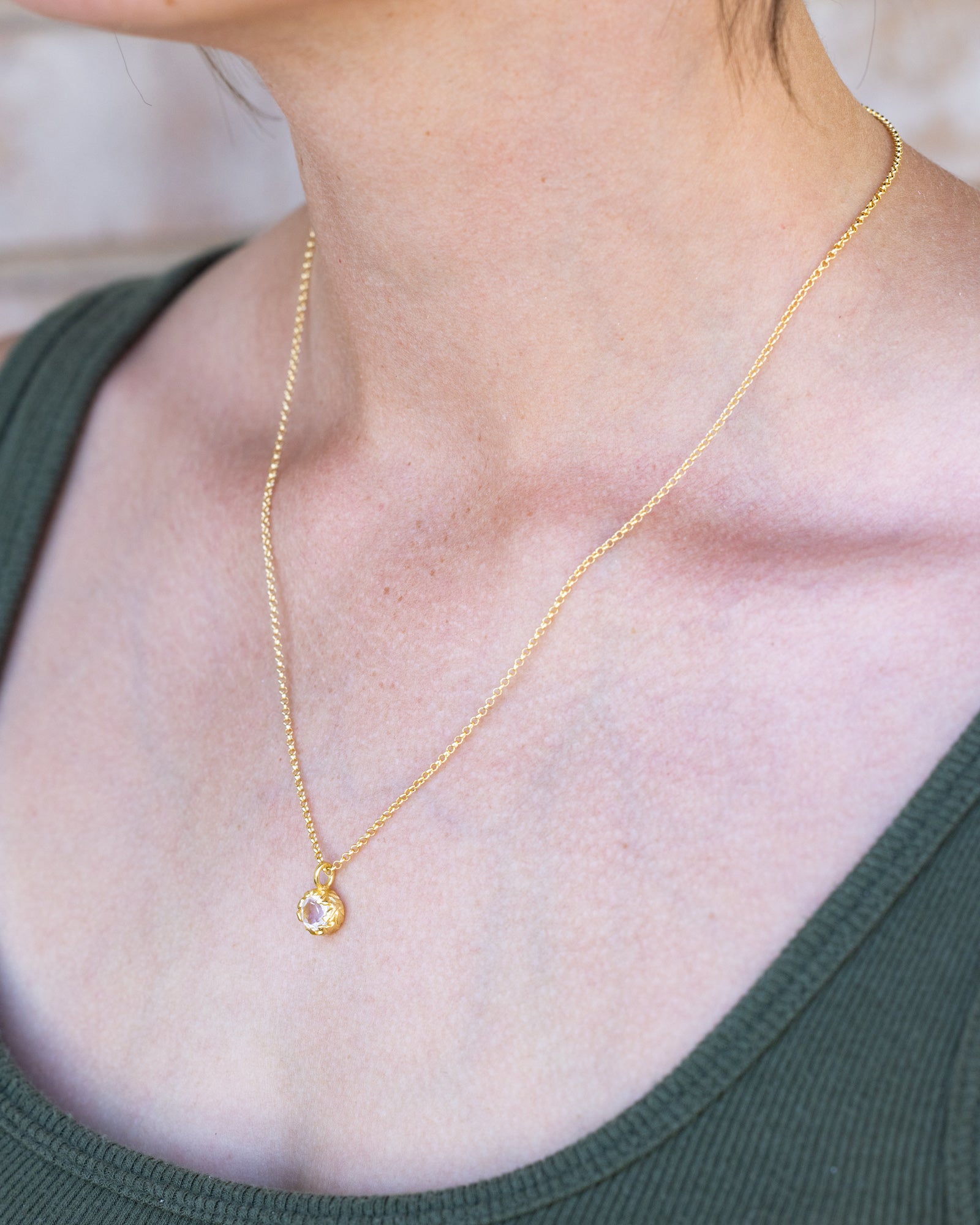 Gold necklace with a white topaz pendant worn by a person in a green top.