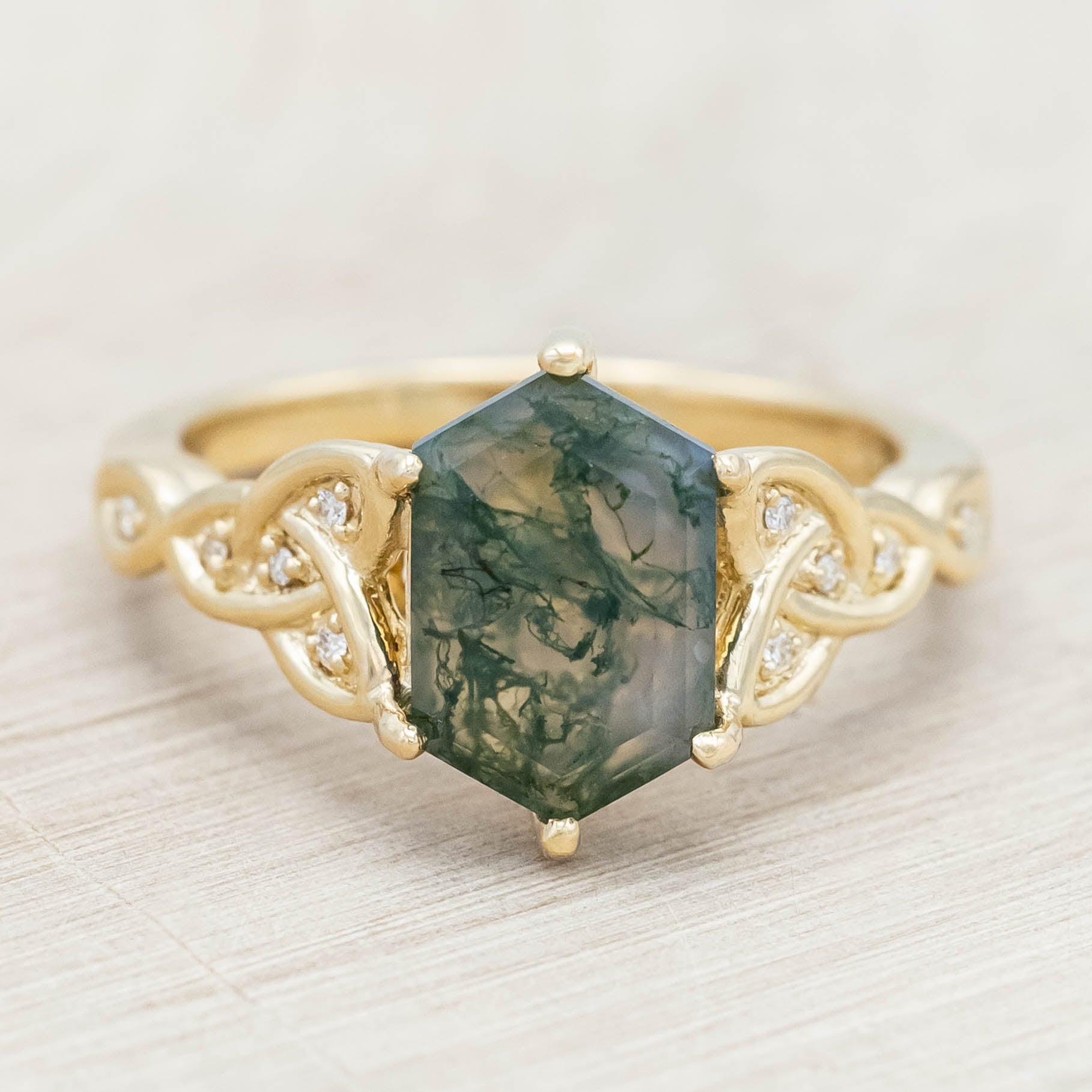 Gold ring with triquetra knot accent and moss agate on a light wooden background