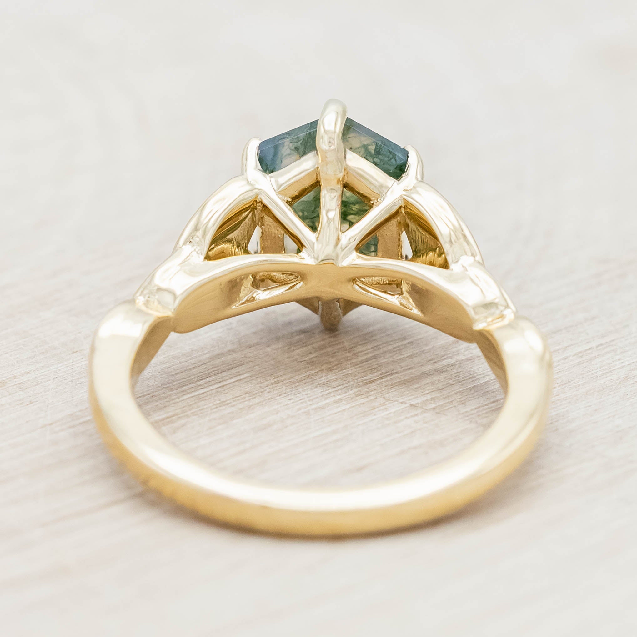 Gold ring with triquetra knot accent and moss agate on a light wooden background