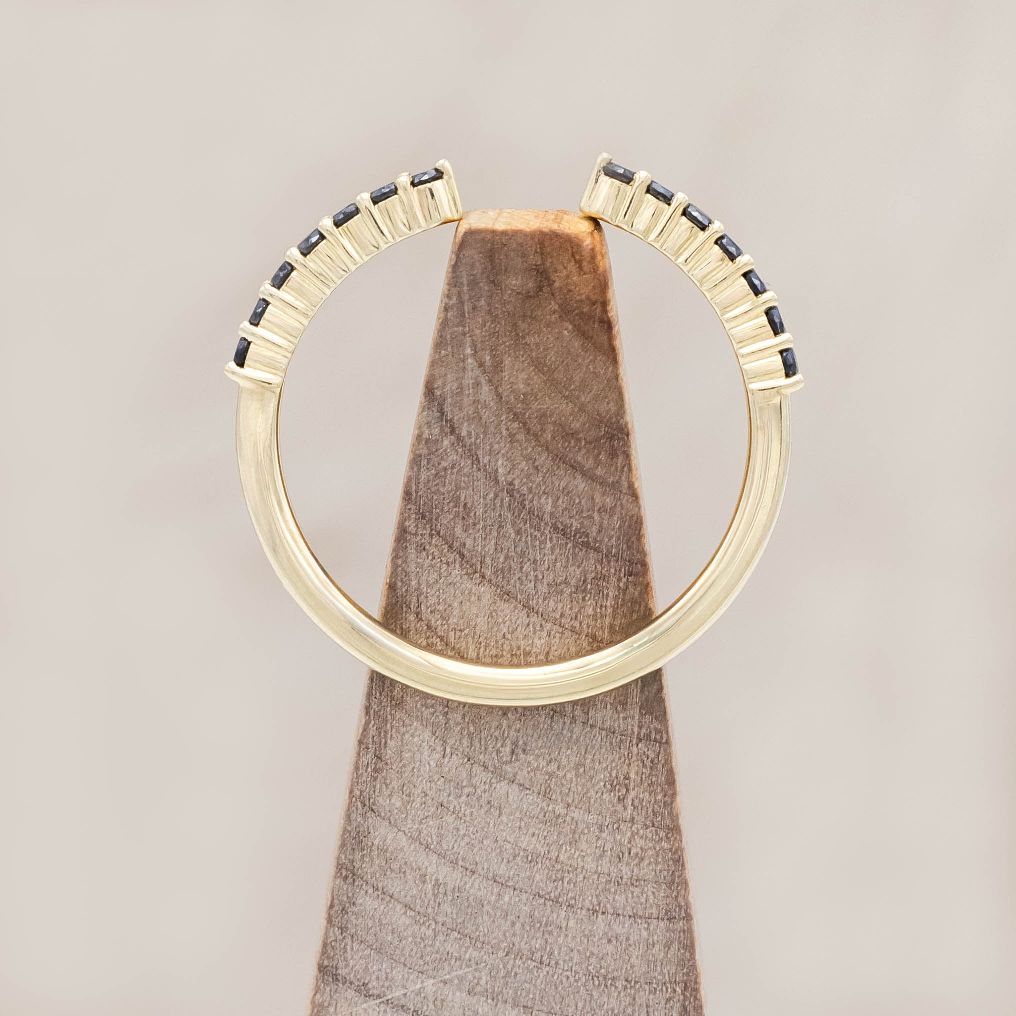 14K yellow gold ring with small black diamonds on a wooden block against a beige background