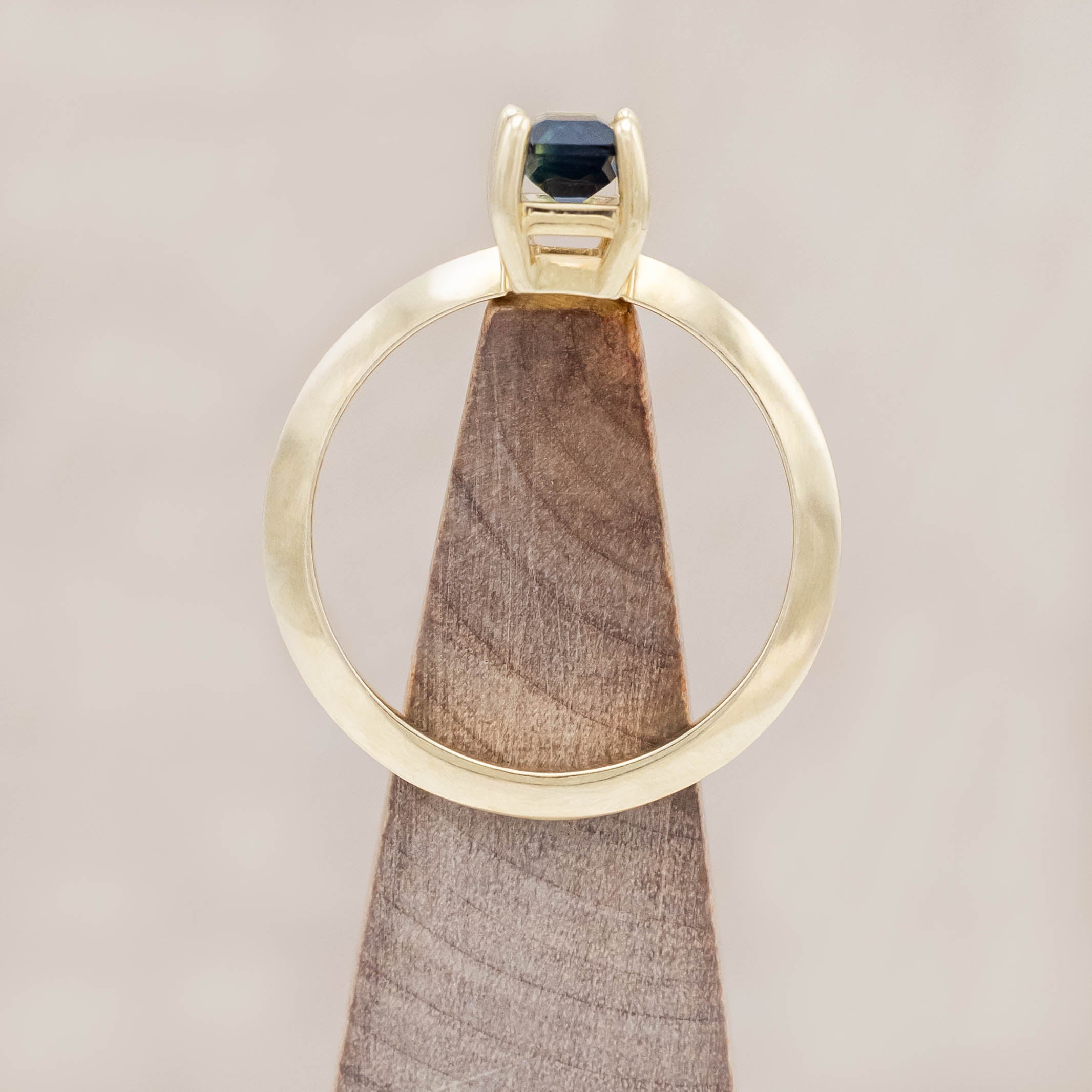 14K yellow gold ring with a green sapphire on a wooden block against a beige background