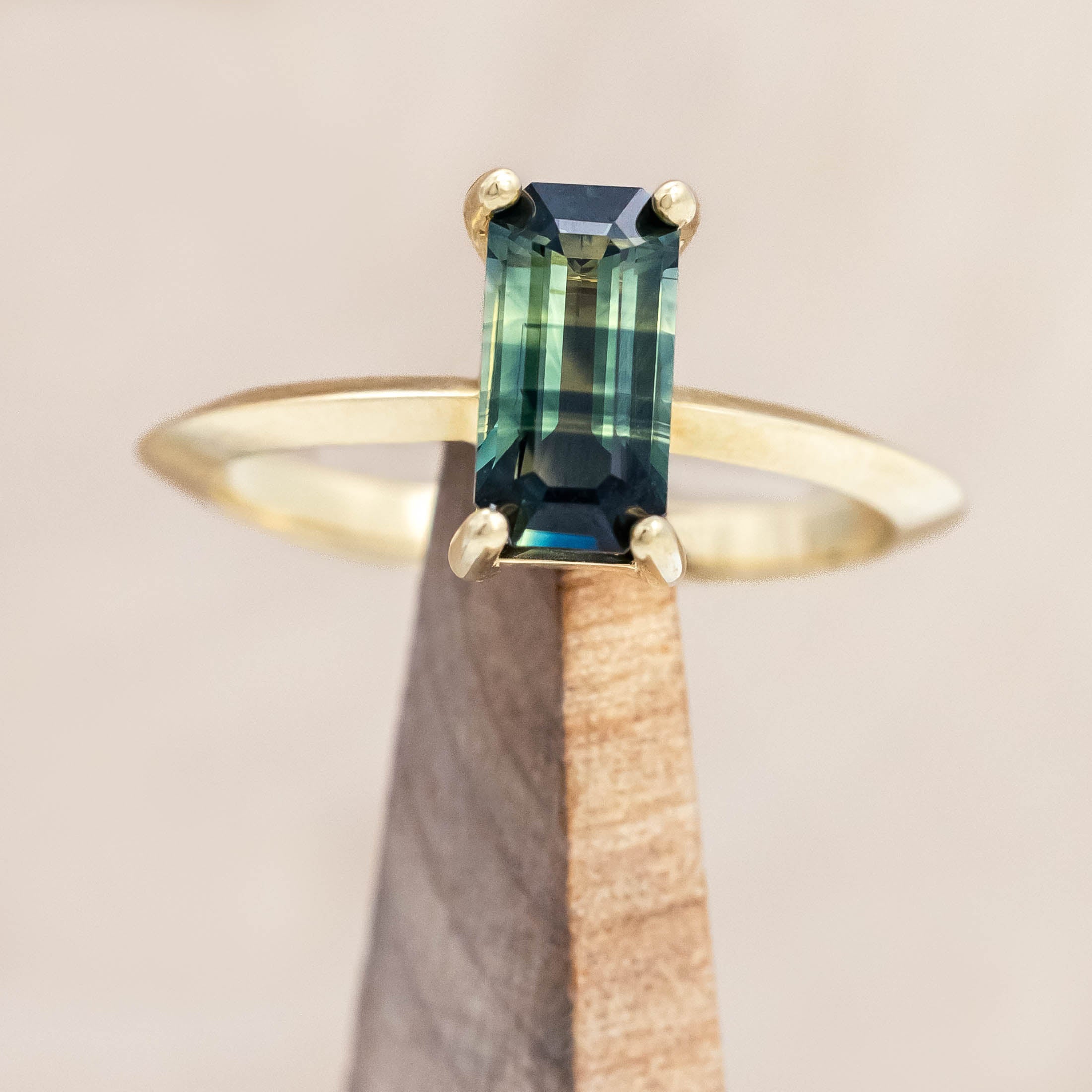 14K yellow gold ring with a green sapphire on a wooden stand against a beige background