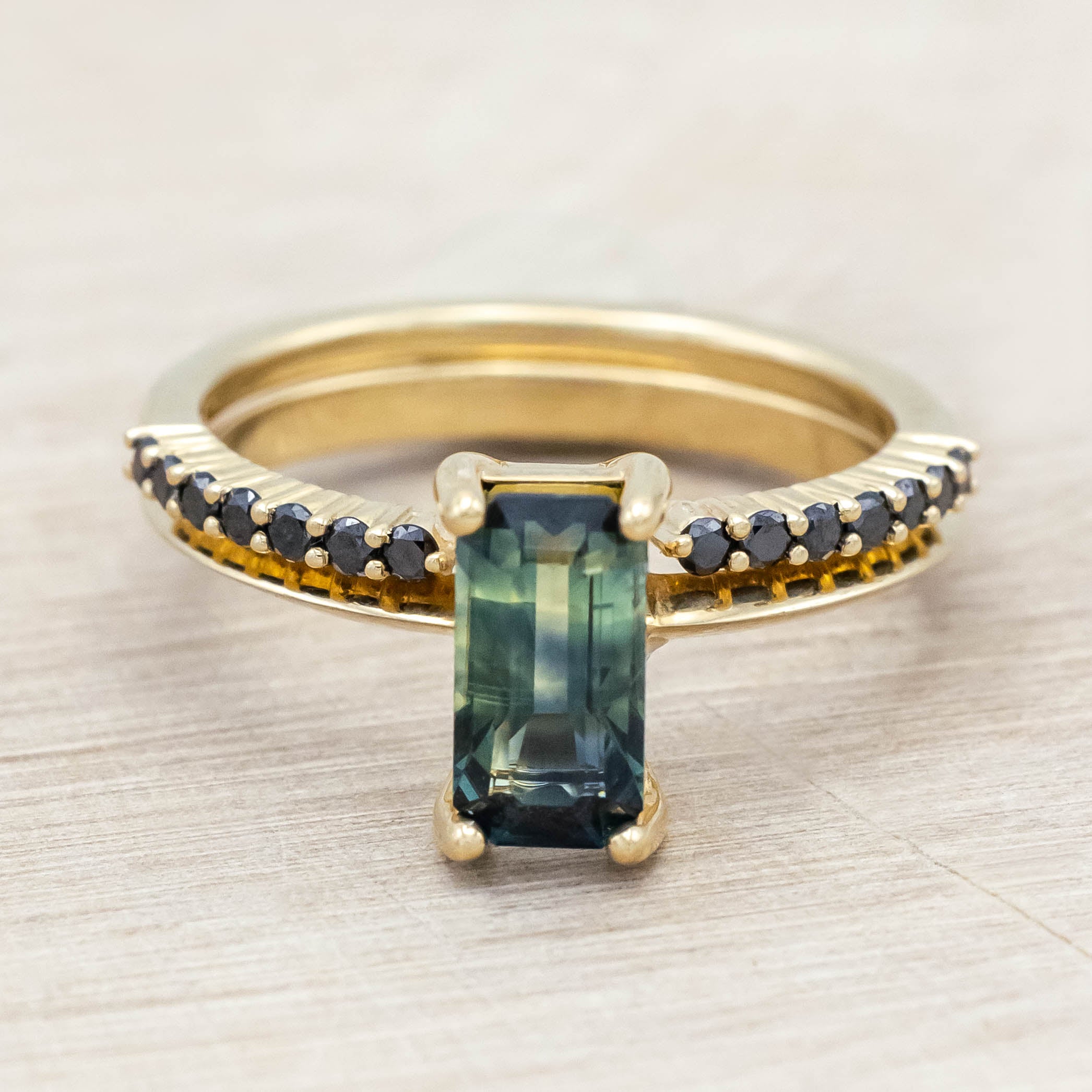 14K yellow gold ring with a green sapphire and black diamond tracer on a light wooden surface