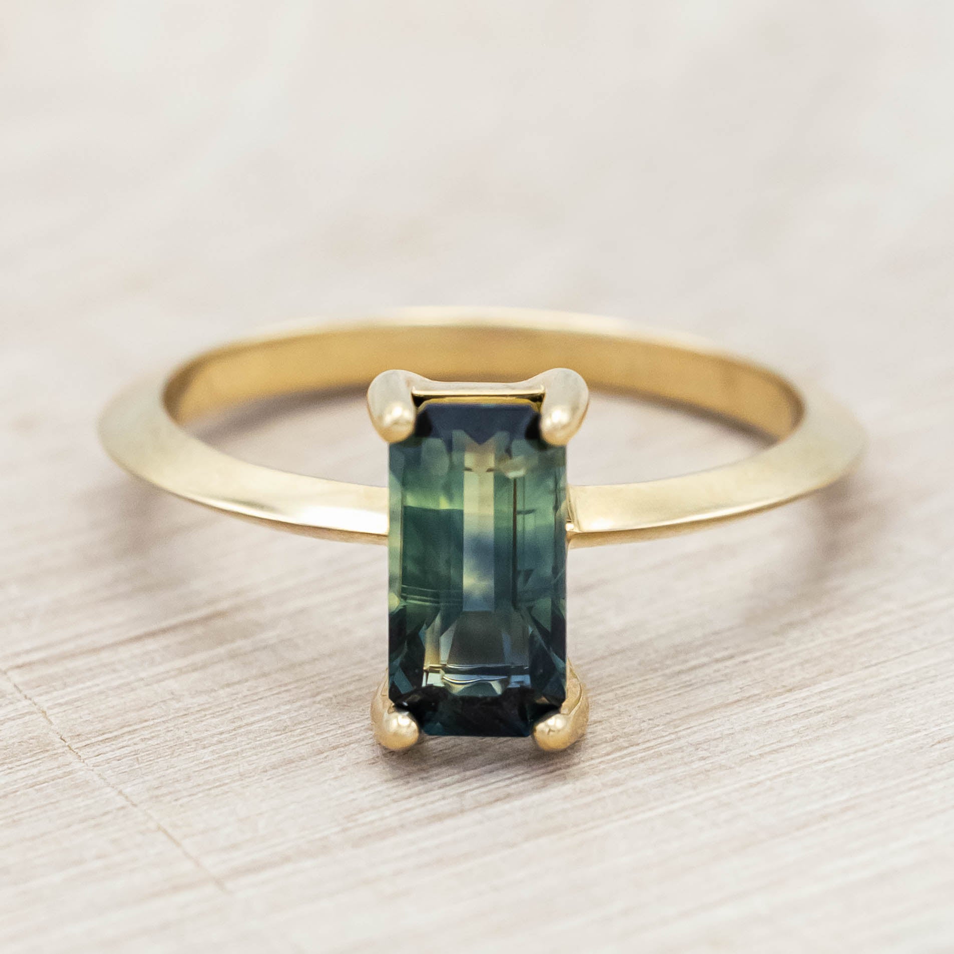 14K yellow gold ring with a green sapphire on a light wooden surface