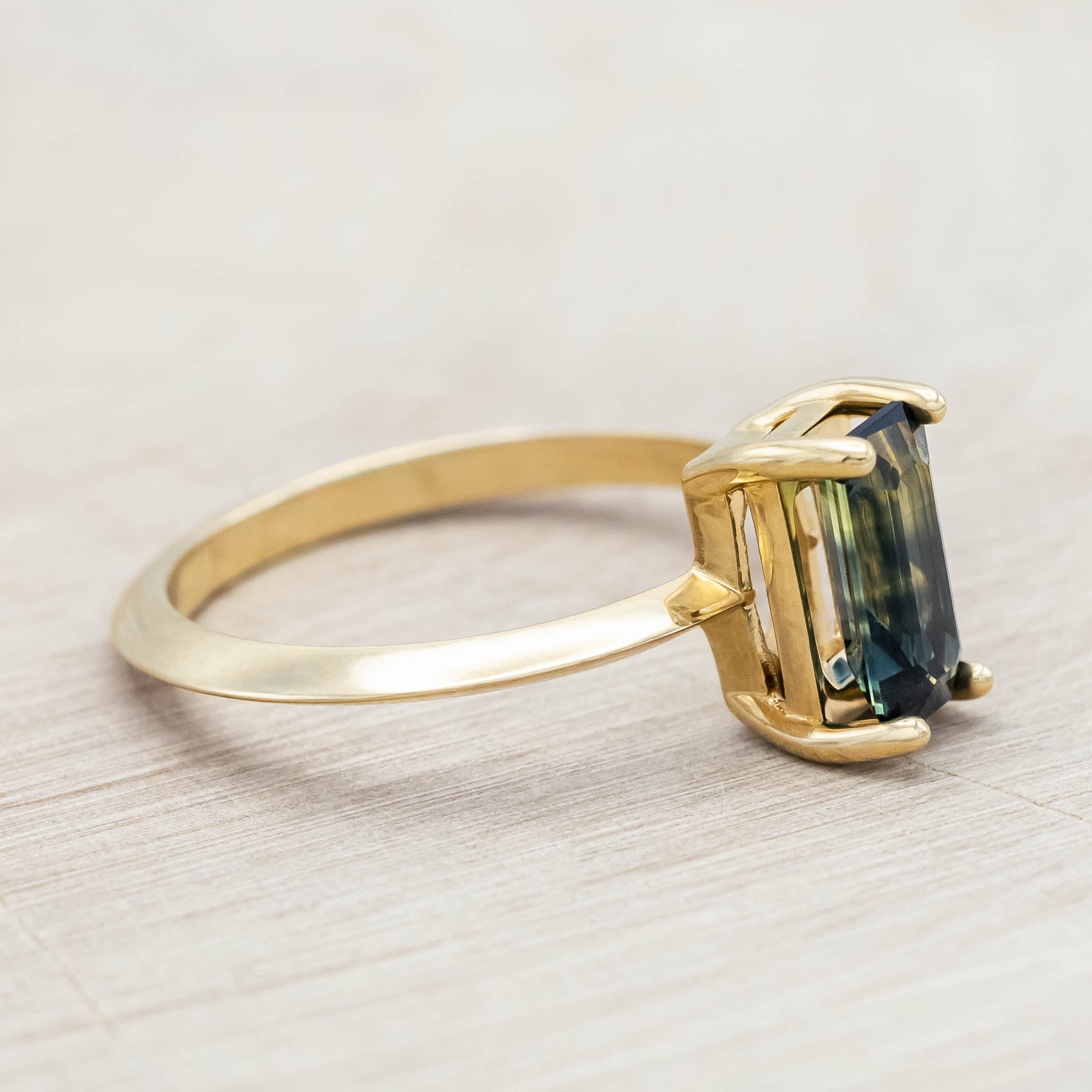 14K yellow gold ring with a green sapphire on a light wooden surface