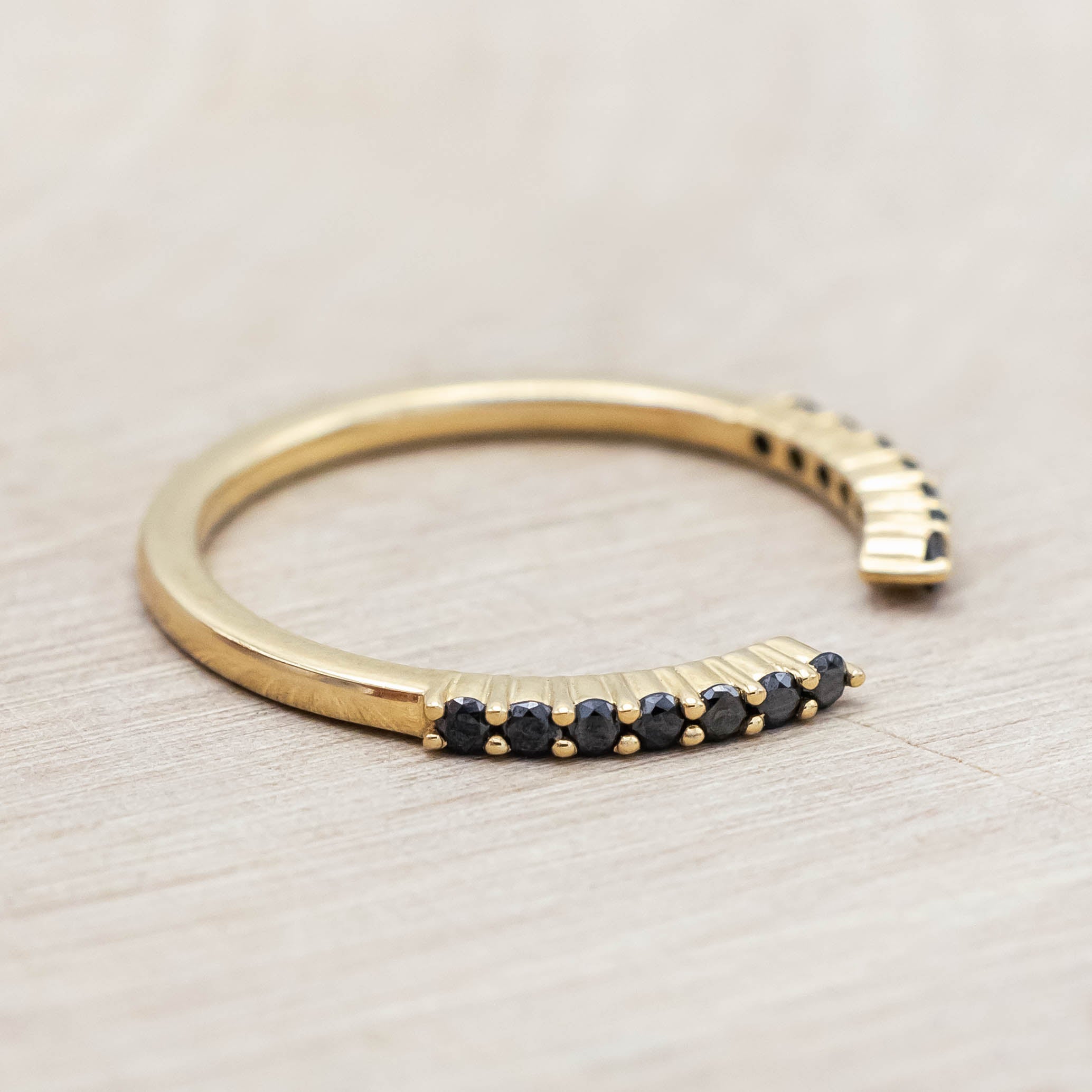 14K yellow gold ring with small black diamonds on a light wooden surface