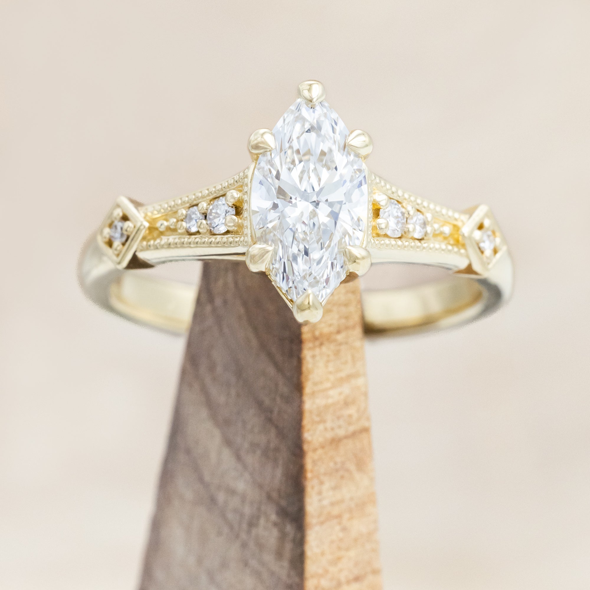14K gold ring with lab-grown diamond center stone & accents on wooden stand against beige background