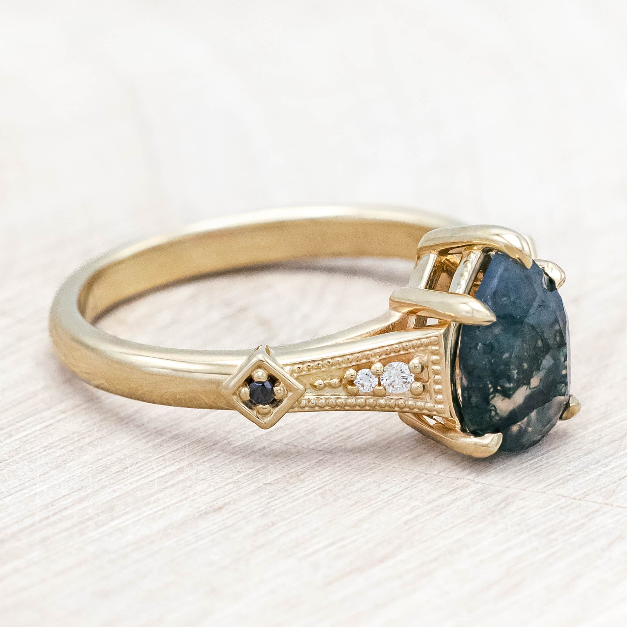 14K gold ring with a moss agate with black and white diamond accents on a wooden stand against a beige background