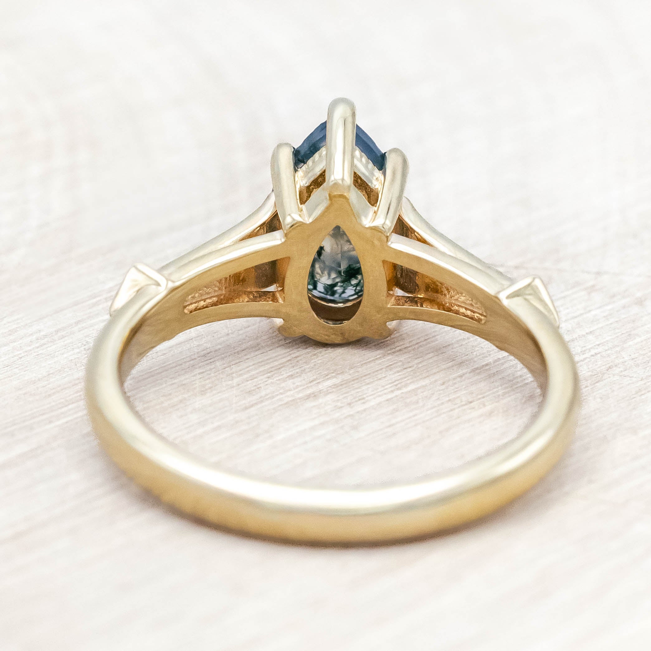 14K gold ring with a moss agate with black and white diamond accents on a wooden stand against a beige background