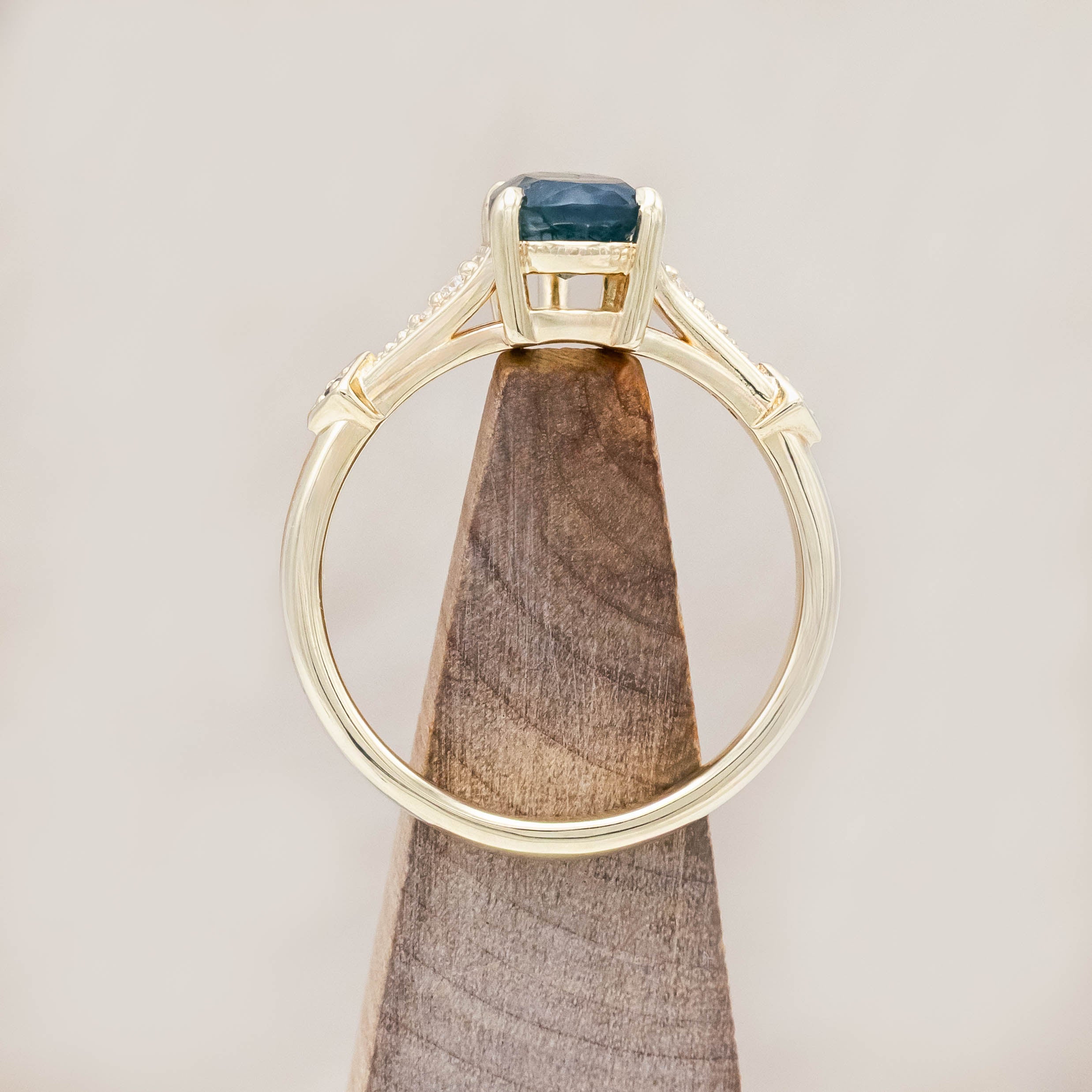 14K gold ring with a moss agate with black and white diamond accents on a wooden stand against a beige background