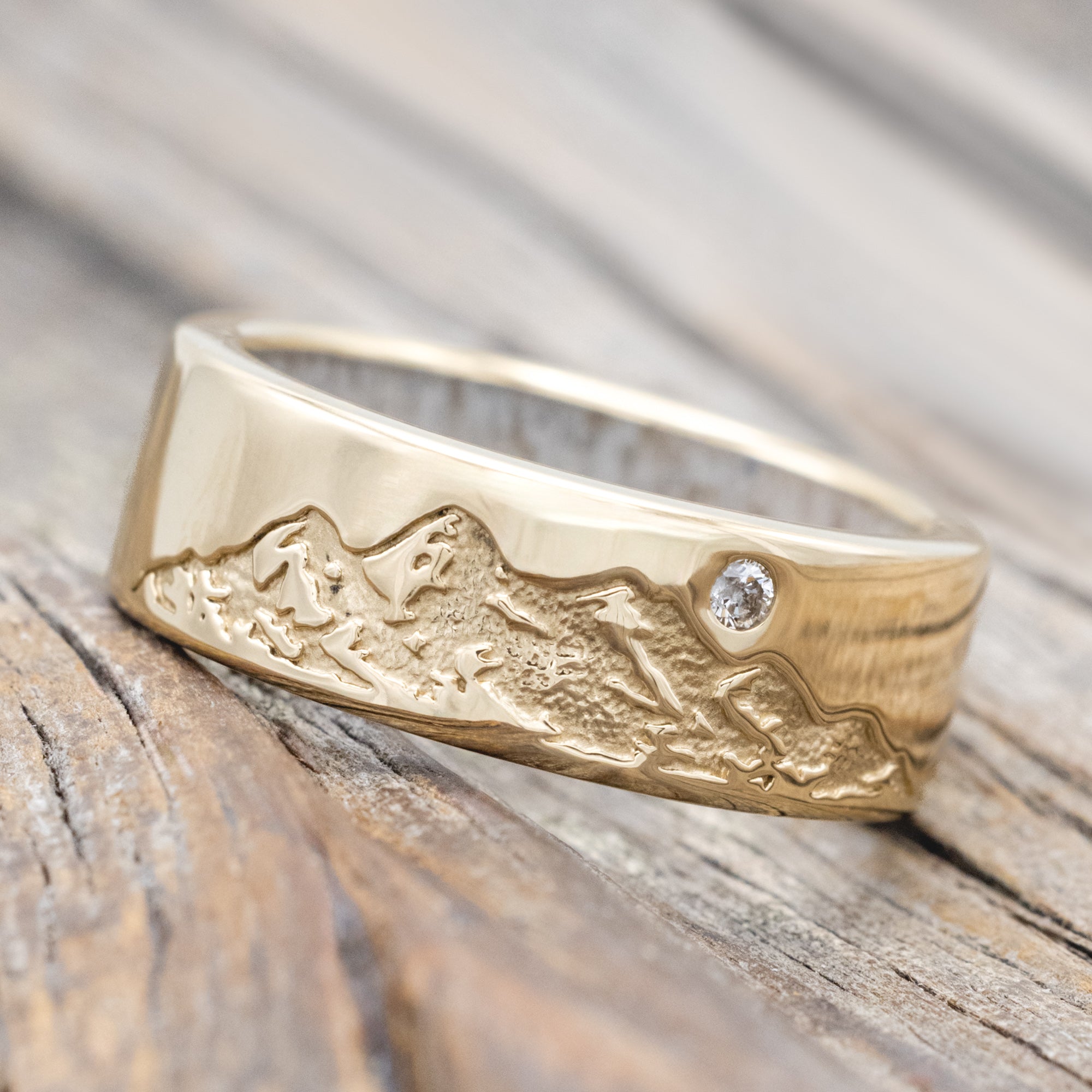 Gold ring with antler lining, diamond accent & mountain engraving on a wooden surface