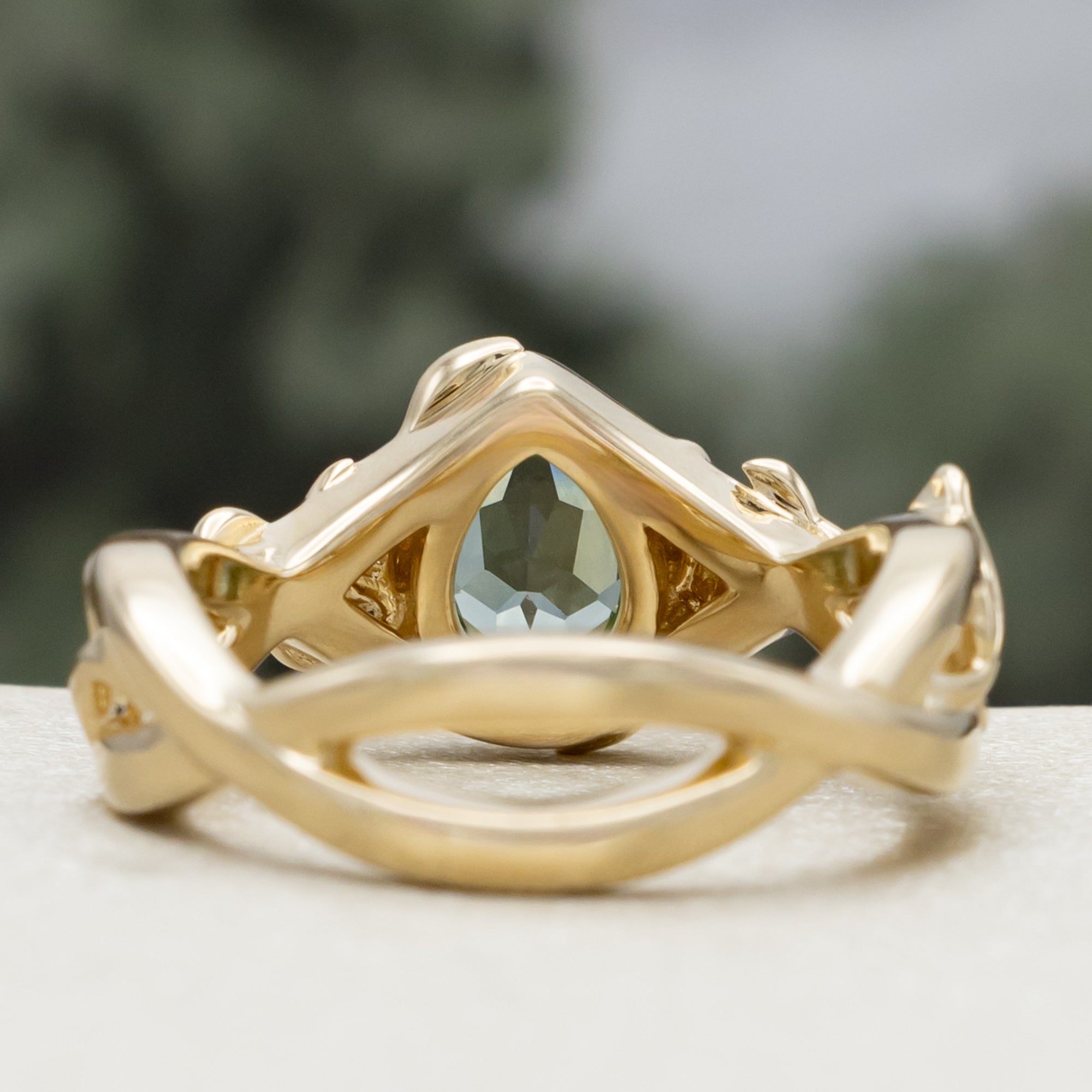 Gold ring with pear lab sapphire and rose/vine accents on a blurred background