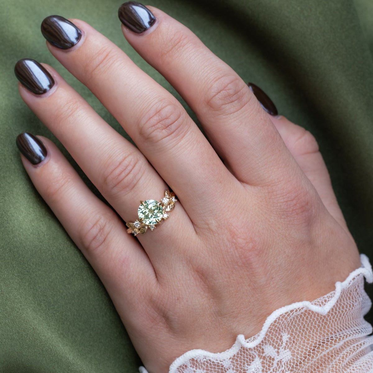 Hand wearing a gold ring with a green sapphire on a green fabric background