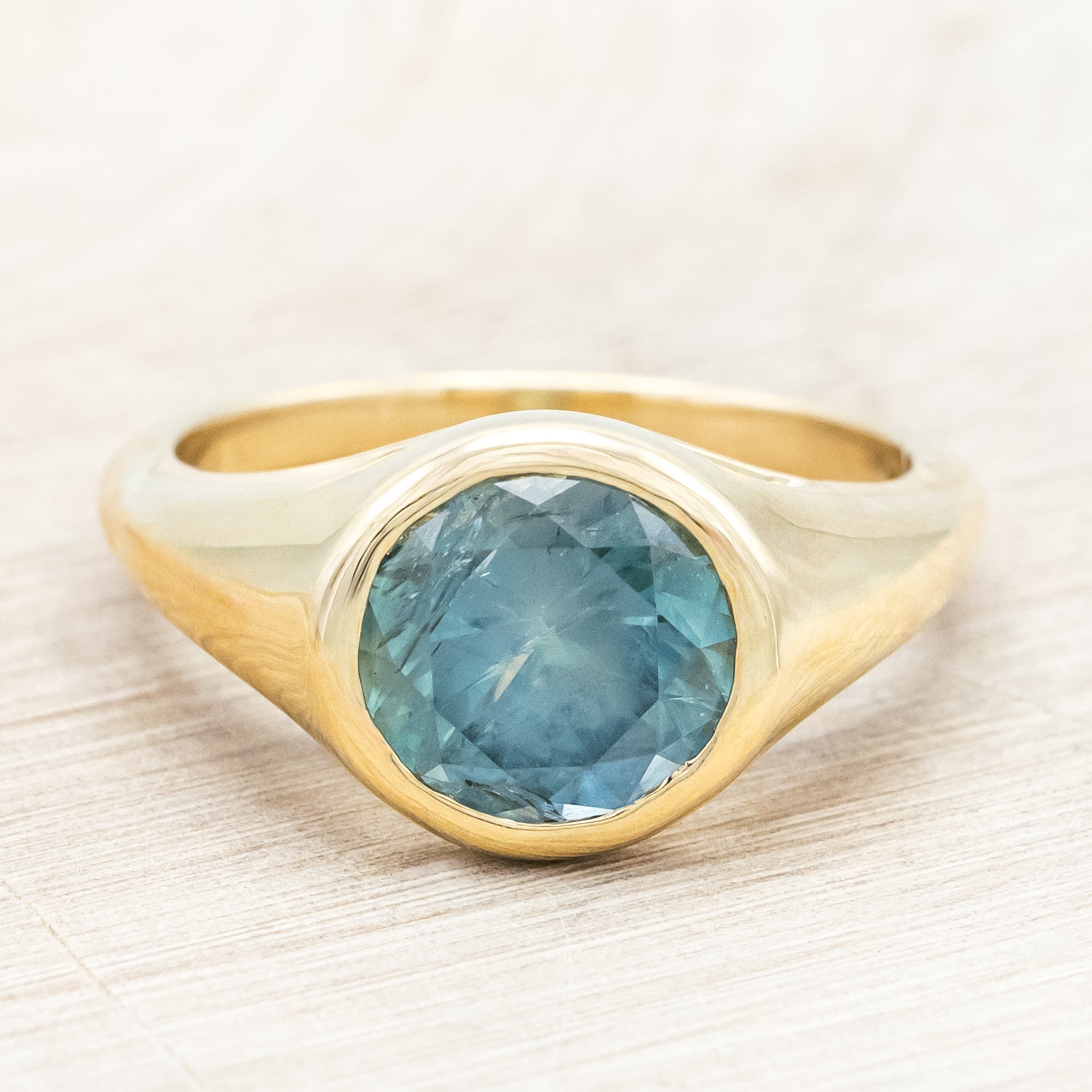 Yellow gold ring with a blue Montana sapphire against a wooden background