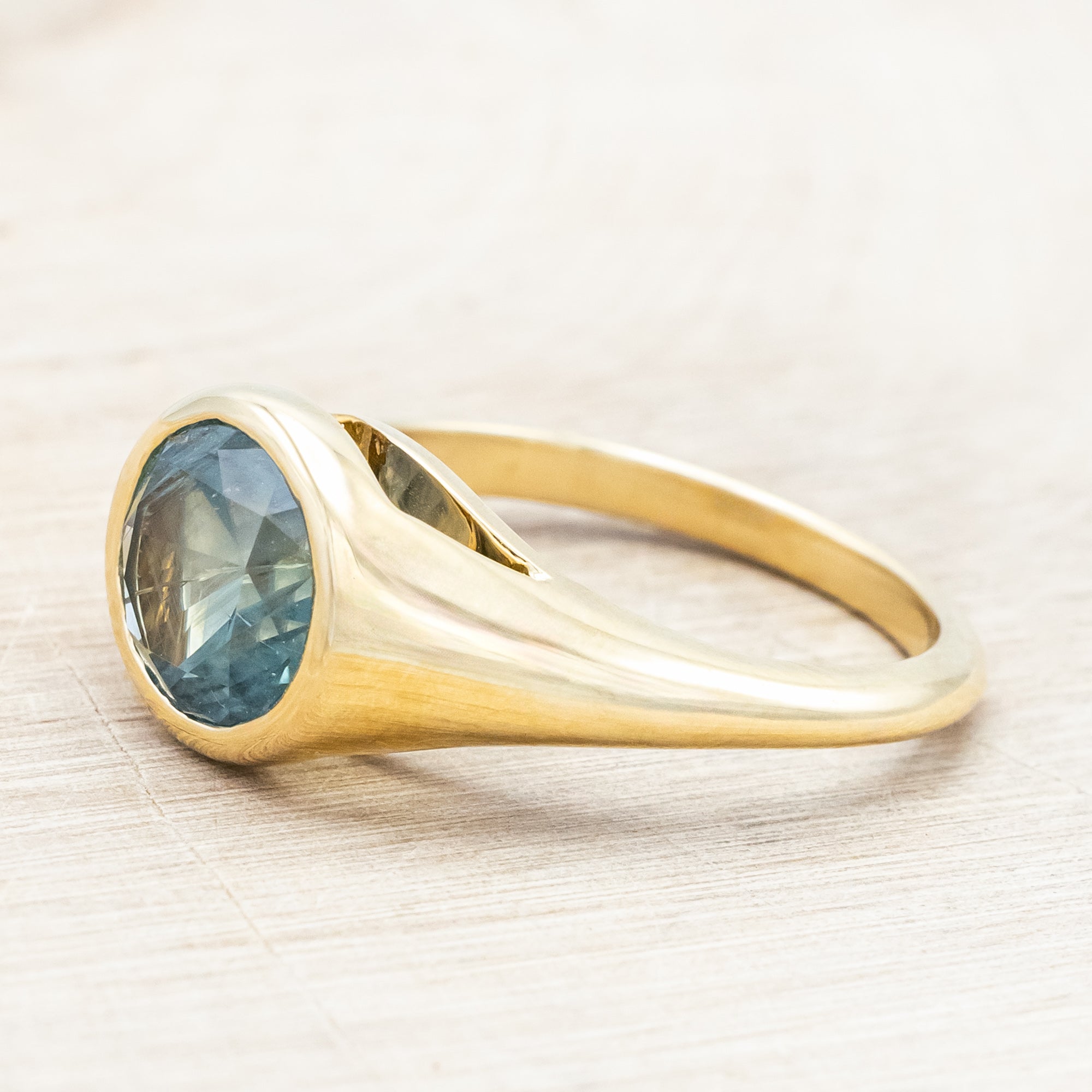Yellow gold ring with a blue Montana sapphire against a wooden background