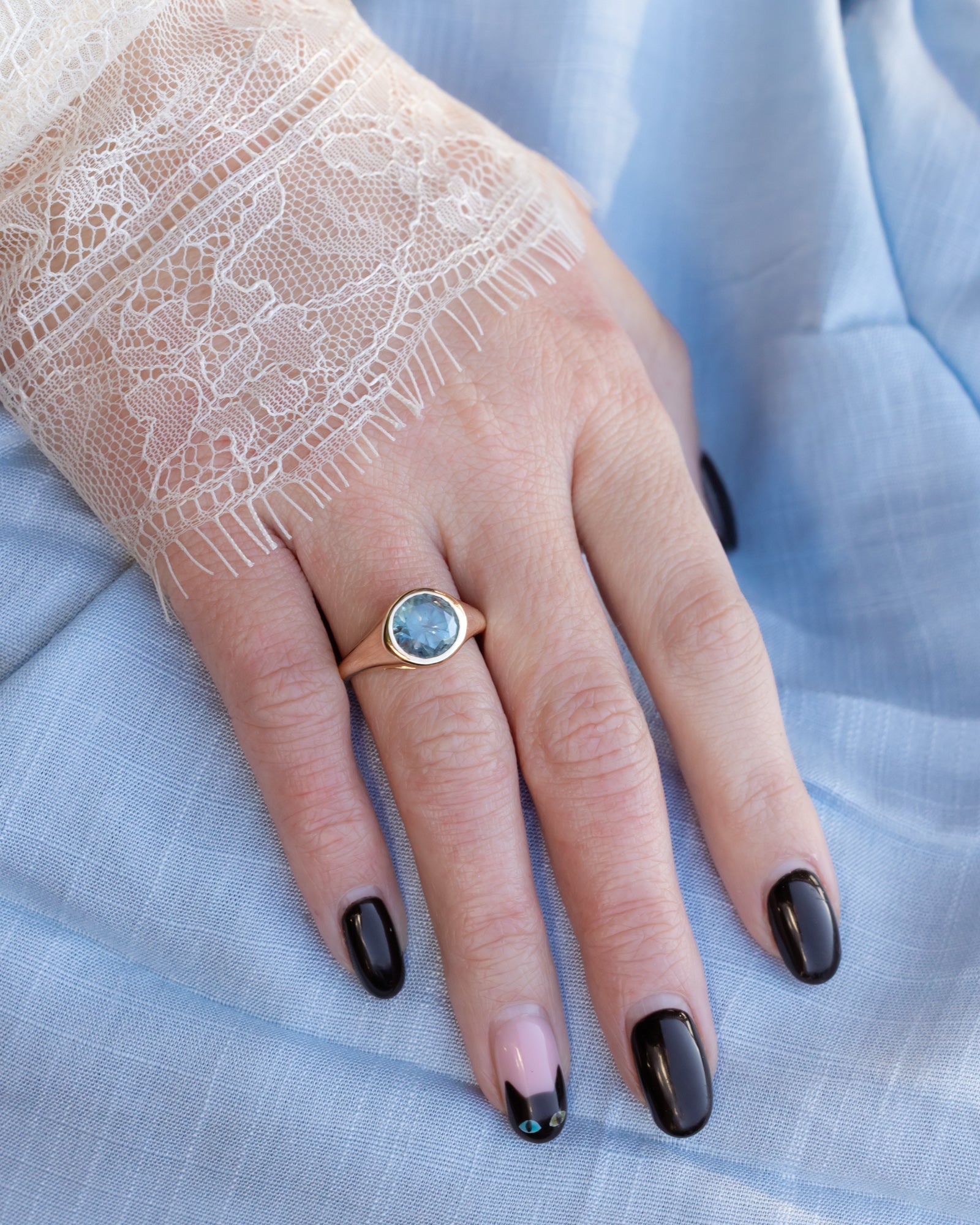 Hand wearing a gold ring with a Montana sapphire on a light blue fabric background