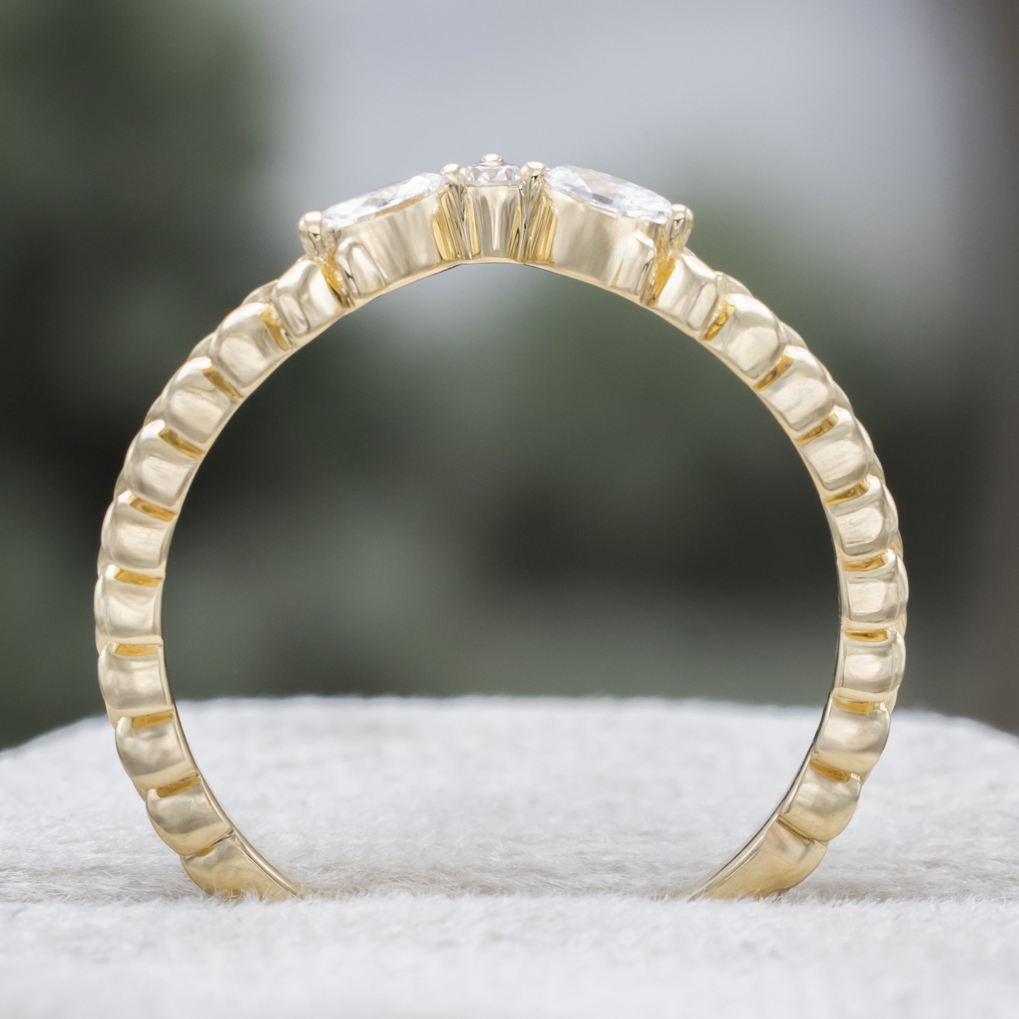 A yellow gold ring tracer with three diamond accents on a vine style band against a blurred green background