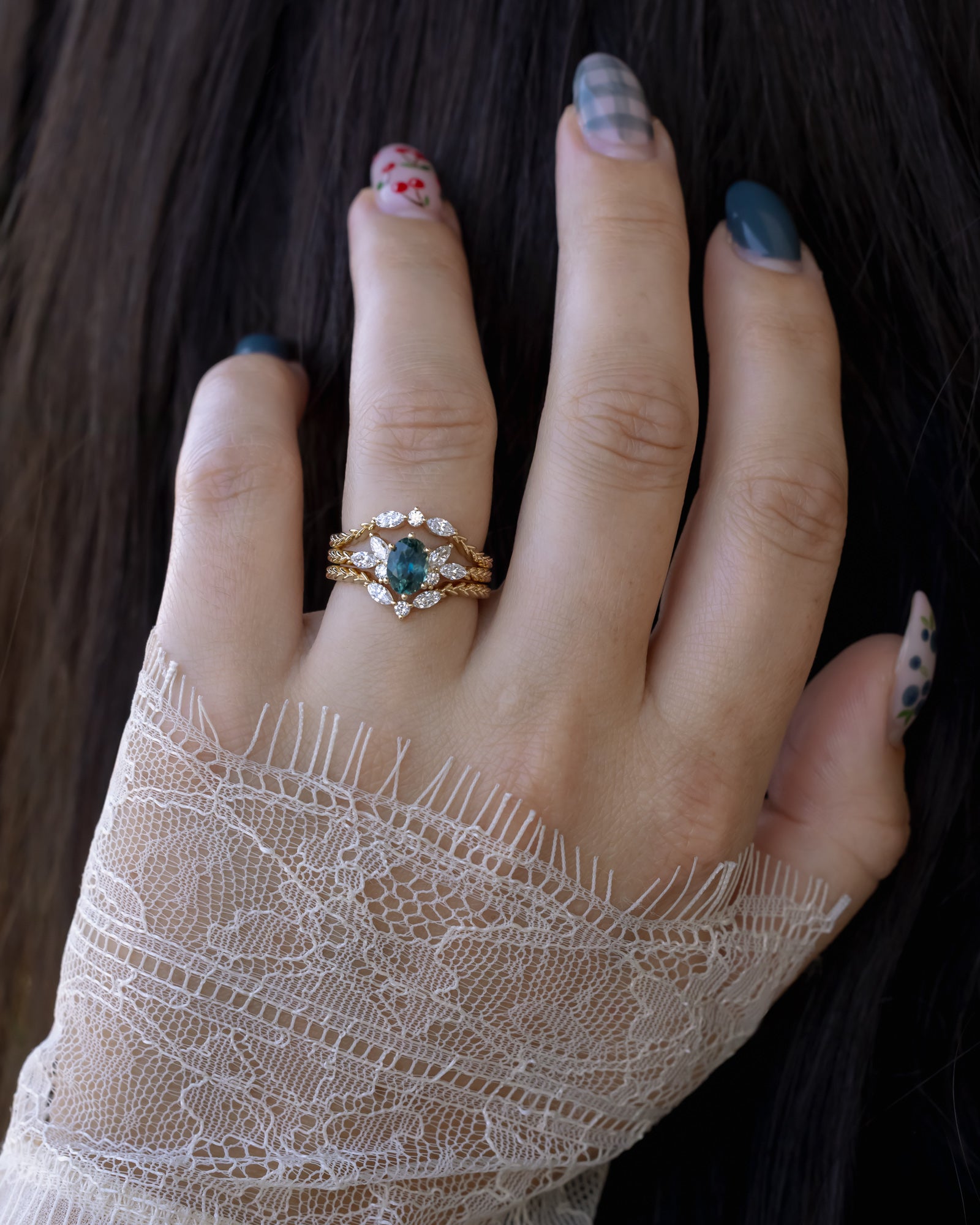 Hand wearing gold ring with oval Montana sapphire with lace sleeve against dark hair