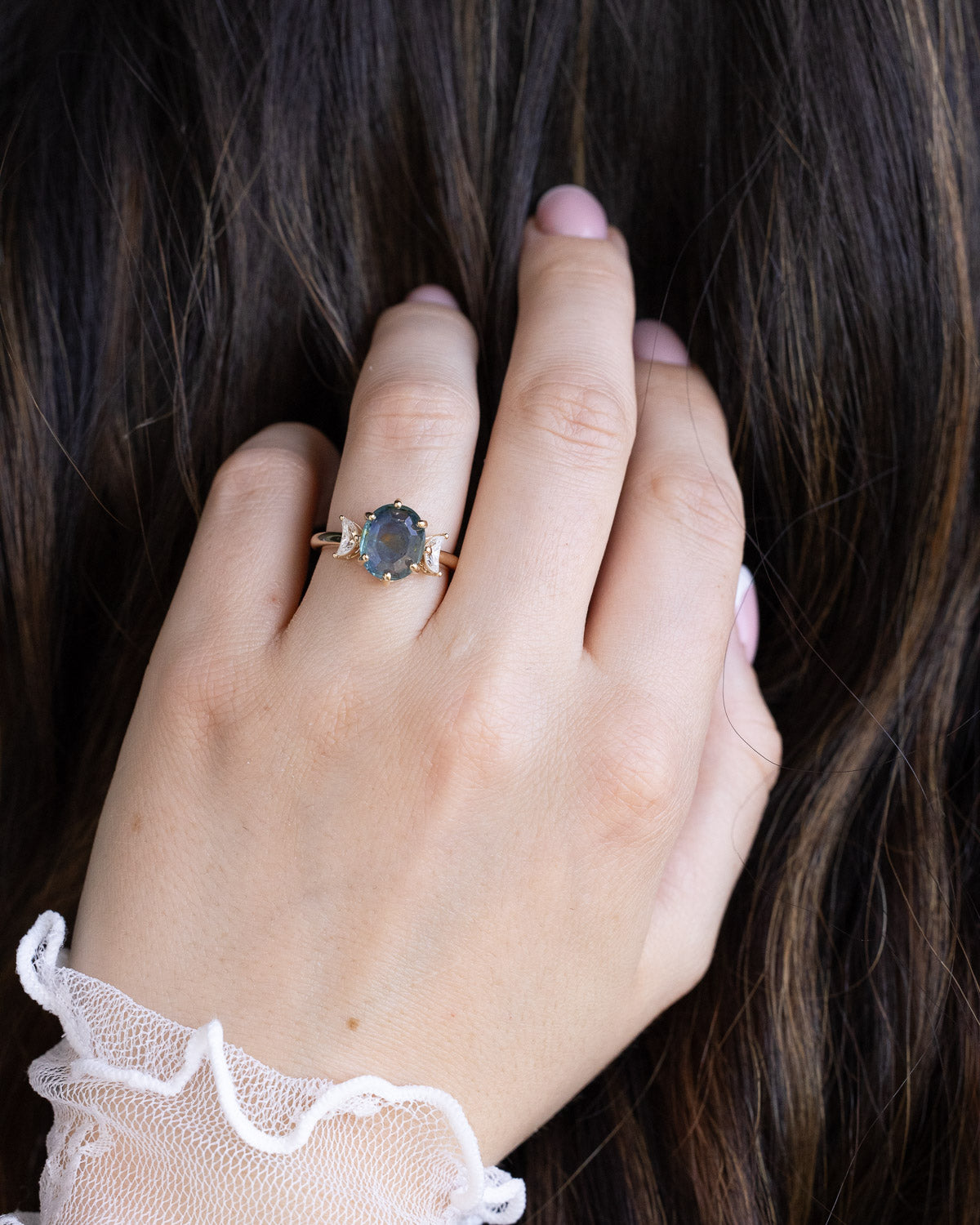 On hand photo of "Rhiannon" engagement ring with a portrait cut Montana sapphire and two crescent moon moissanite accents