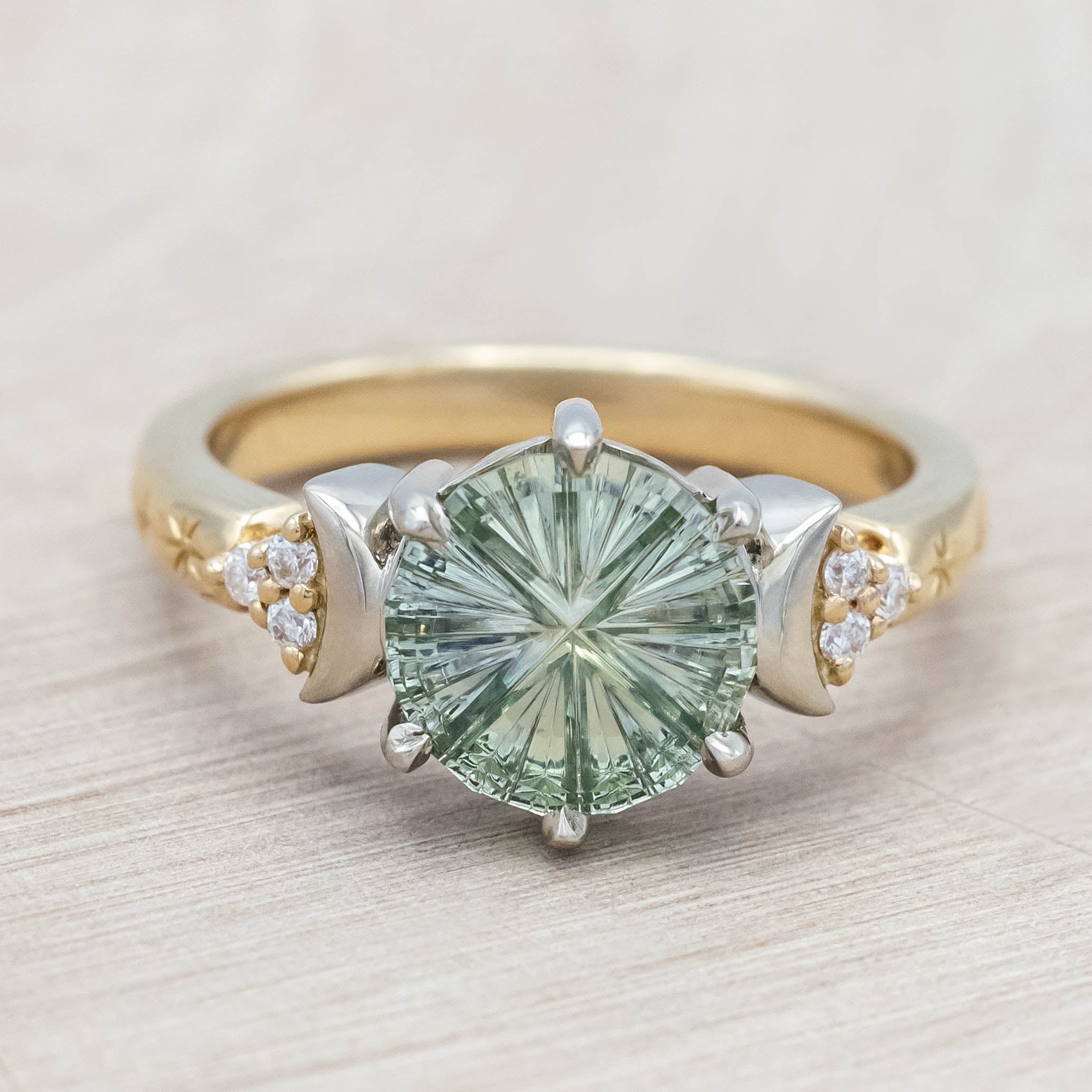Gold ring with a green sapphire and crescent moon accents on a light wooden surface