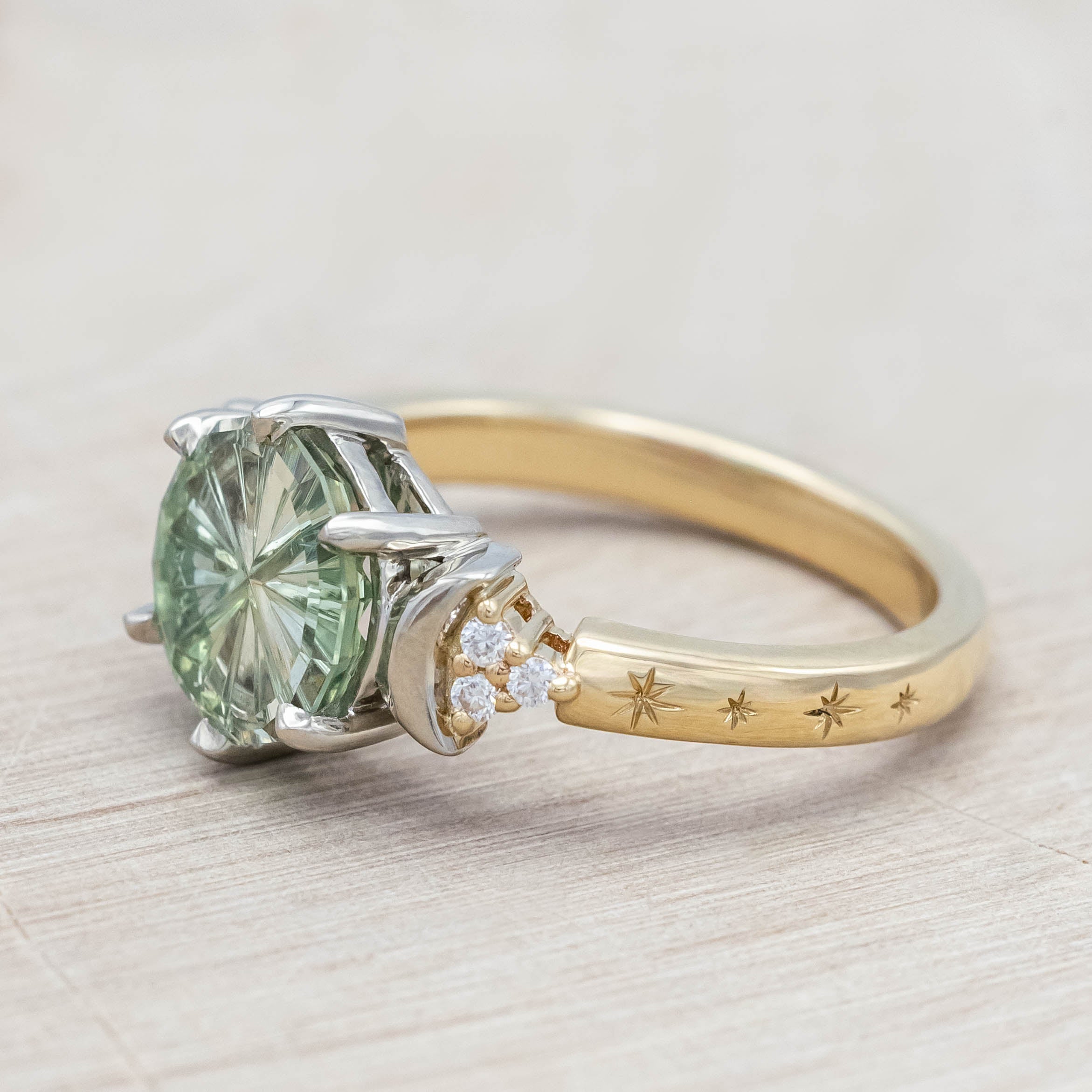 Gold ring with a green sapphire and crescent moon accents on a light wooden surface