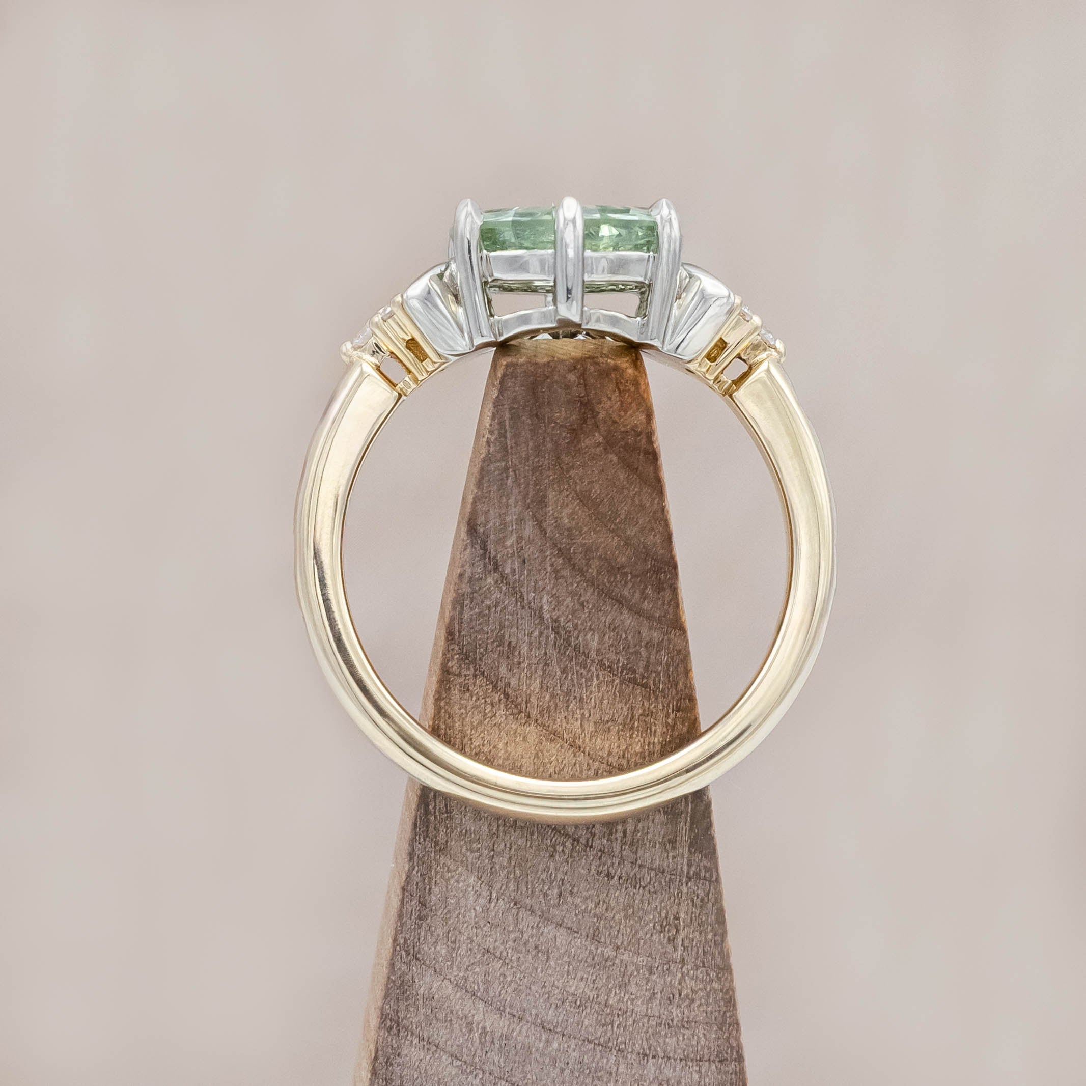 Gold ring with a green sapphire and crescent moon accents on a wooden block against a beige background